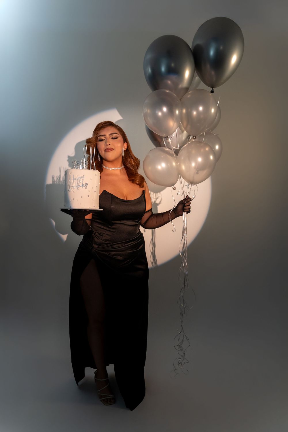 Studio birthday portrait with spotlight lighting, birthday cake and silver balloons in Miami.