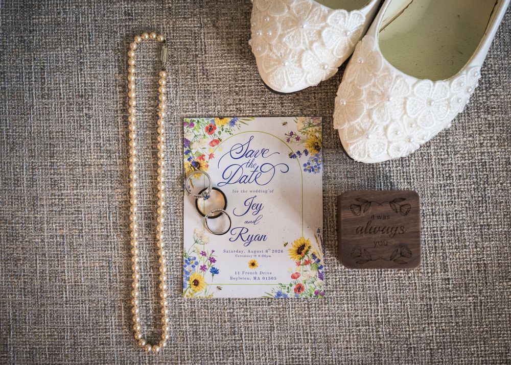 Wedding flat lay featuring save the date card, pearl necklace, rings, lace shoes, and ring box.