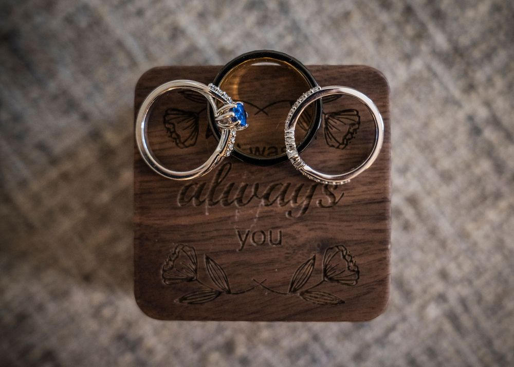 Three wedding rings rest on an engraved wooden ring box with the phrase always you and angel wing designs.