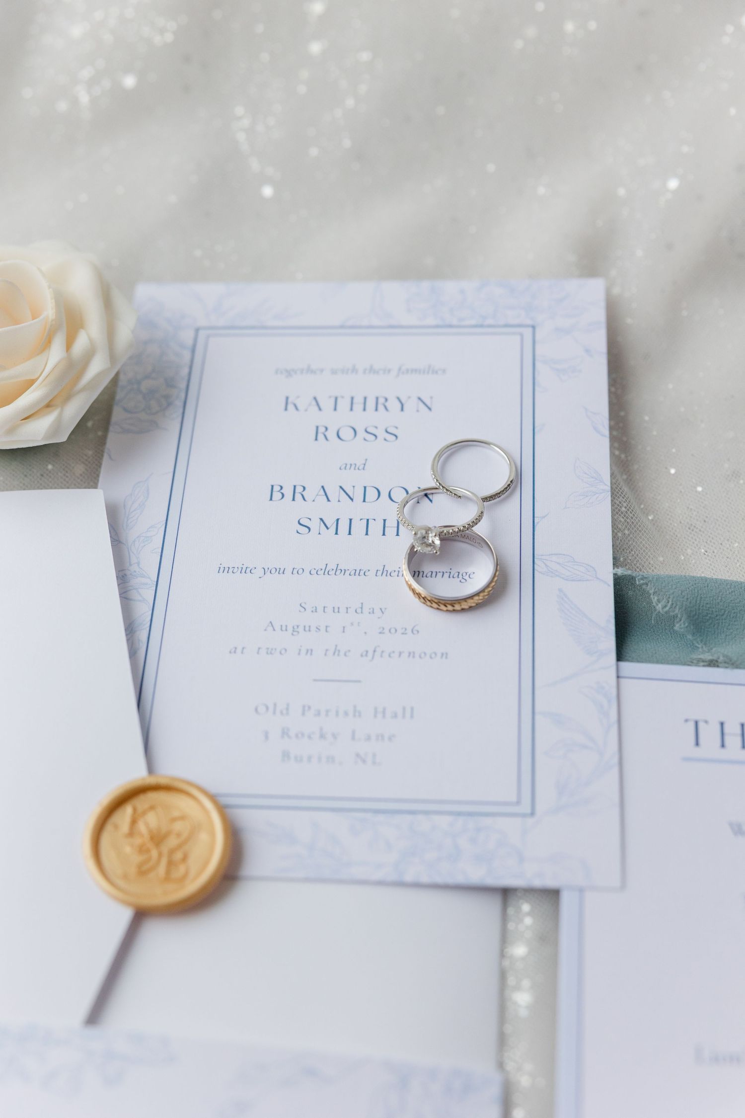 Elegant wedding invitation for Kathryn Ross and Brandon Smith with gold wax seal and diamond rings on white fabric.
