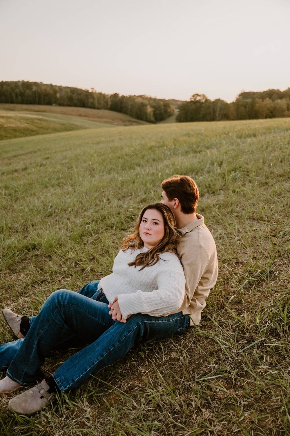 Couple relaxing on a grassy hillside at sunset, woman leaning back against her partner outdoors, couples photo session NC