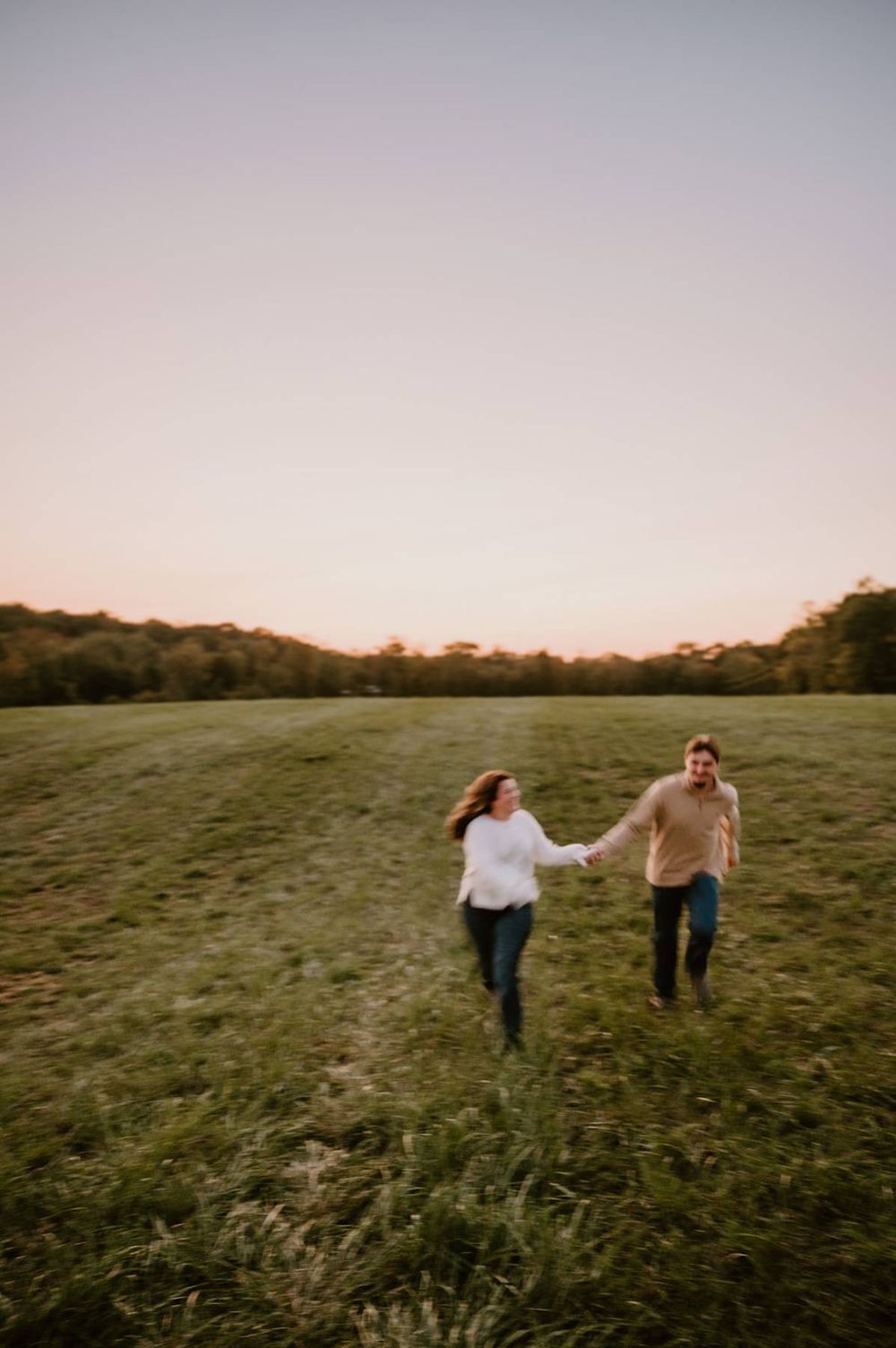 Couple running hand in hand through open green field at golden hour with glowing sunset sky, couples photographer in North Carolina