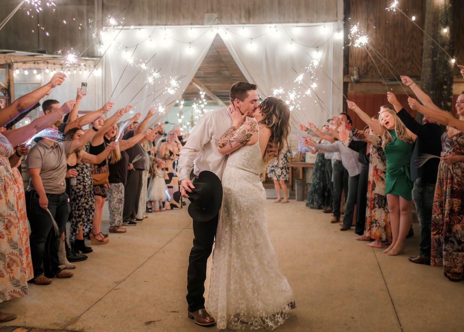 Bride and groom share a kiss during a sparkler sendoff at their rustic barn wedding reception at night.