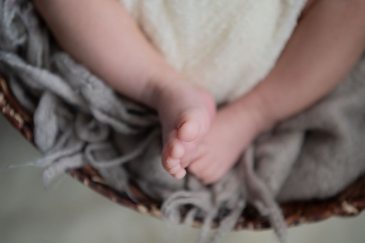 Black and white photo of a sleeping newborn baby wrapped in a soft blanket inside a woven basket.