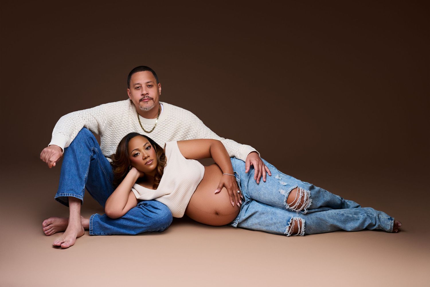 Couple poses for maternity photo shoot, woman lying down showing baby bump, man sitting behind her. NJ Maternity Photographer Gricel's Photo