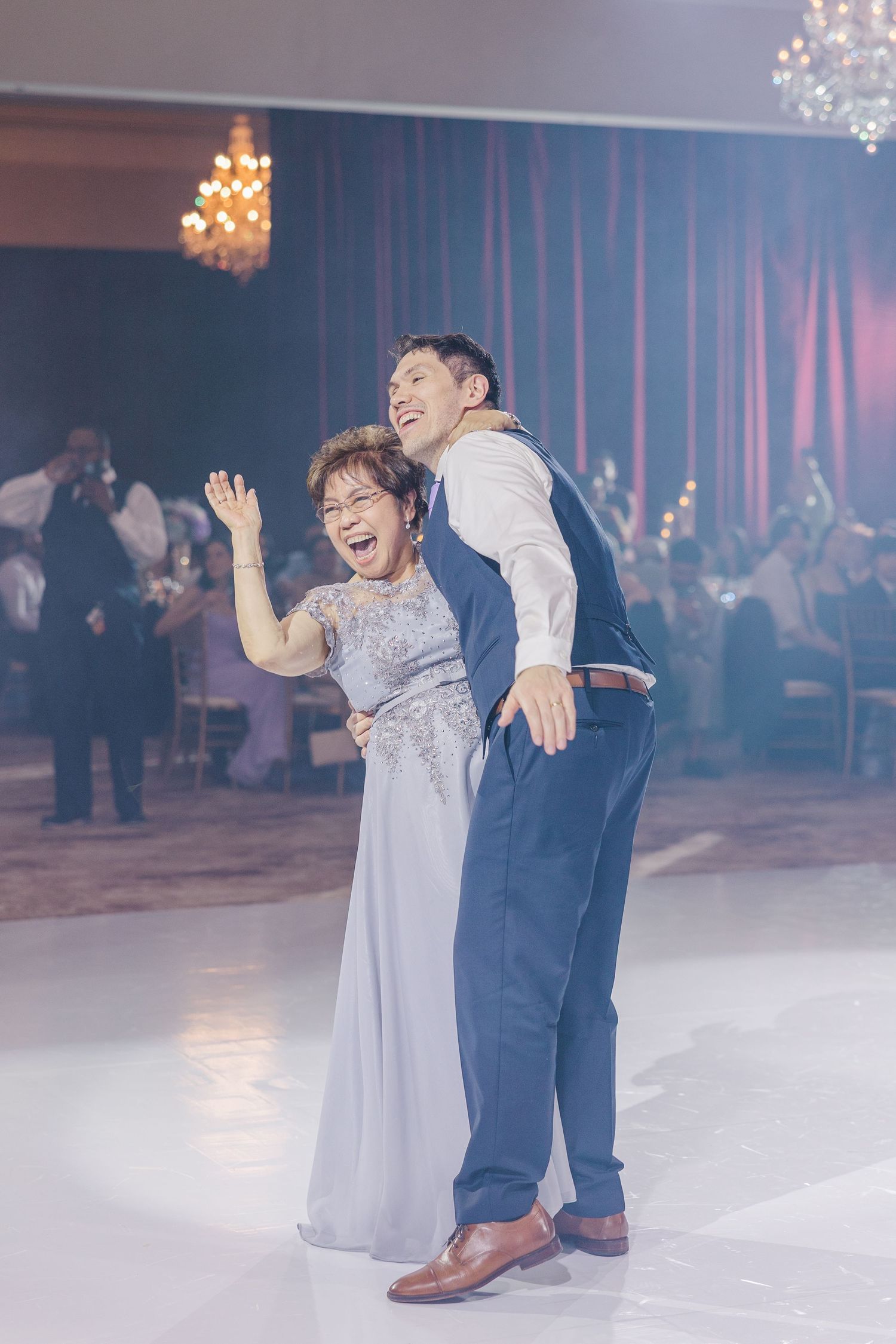 A joyful mother and son share a lively dance together on a wedding reception dance floor.