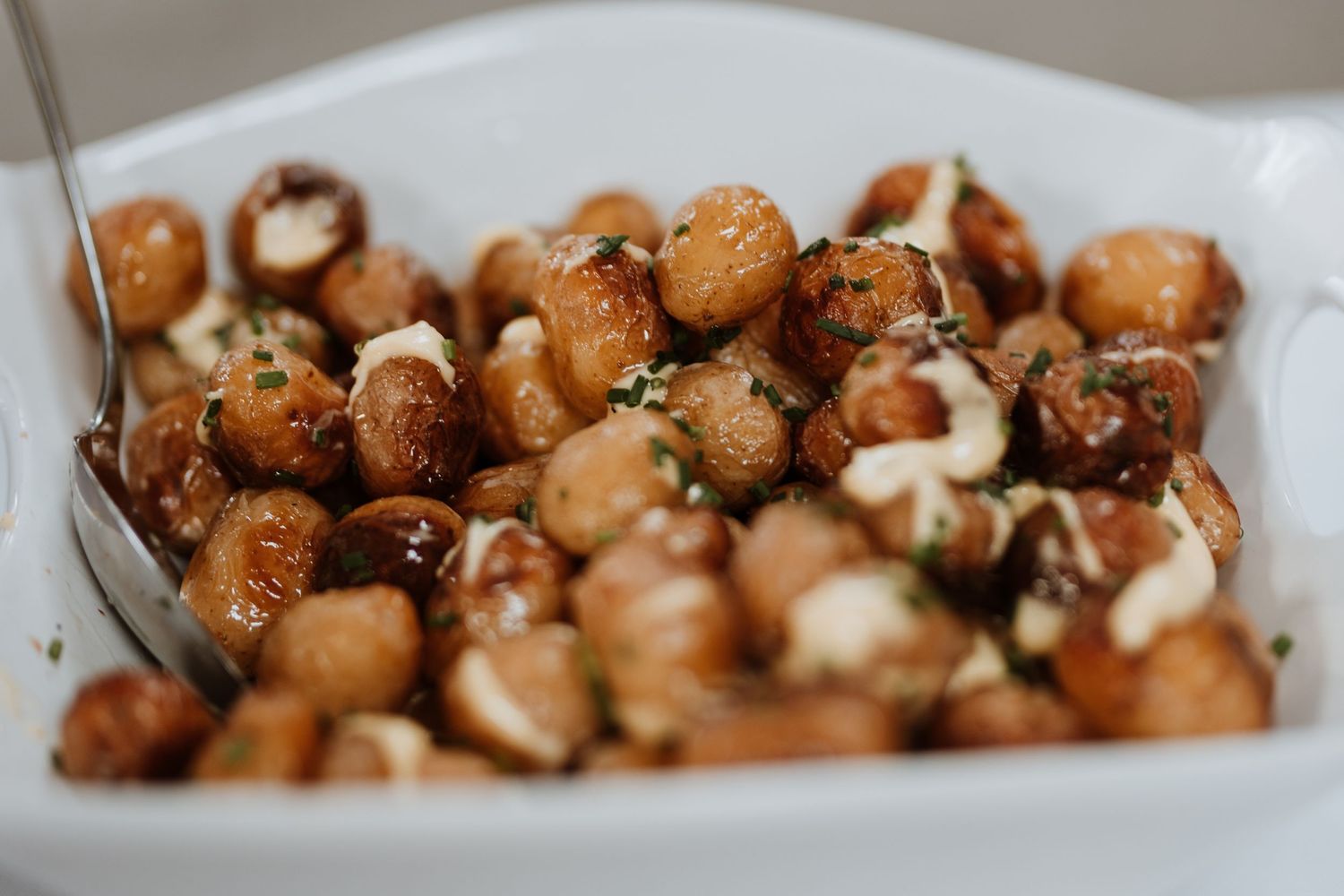 Roasted potatoes with fresh herbs and garlic served in a white ceramic dish with a spoon.