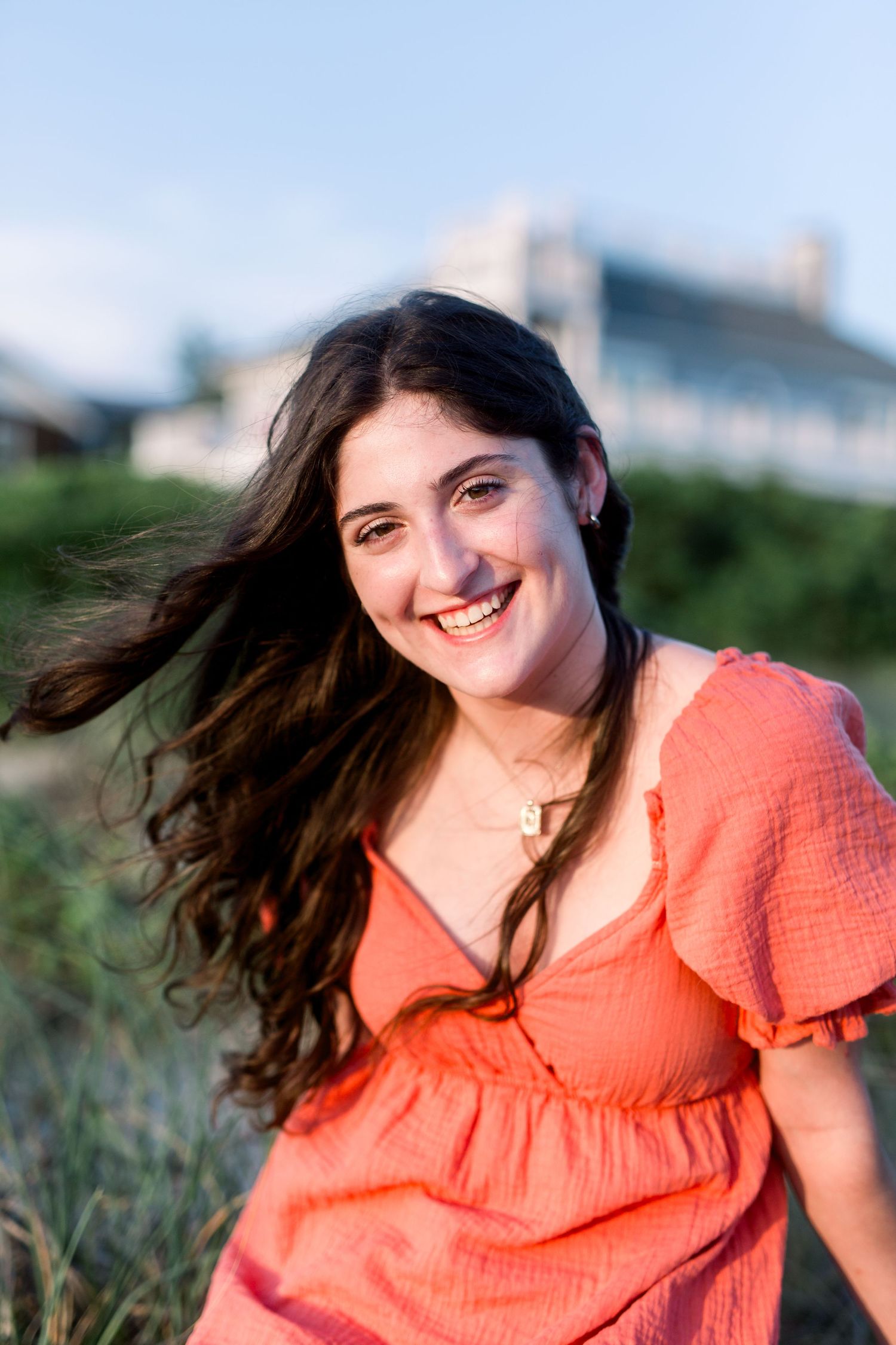 Summer outdoor portrait in a coral dress with coastal beach houses visible in the background.