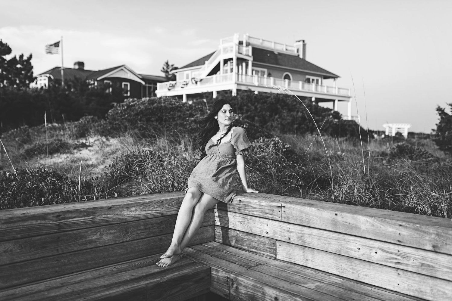 Black and white photo of someone on wooden steps with a coastal house visible on the hilltop.