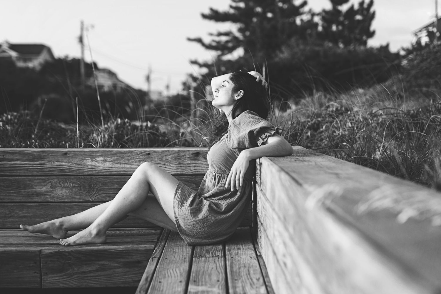 Black and white image of someone in vintage dress reclining on wooden boardwalk.