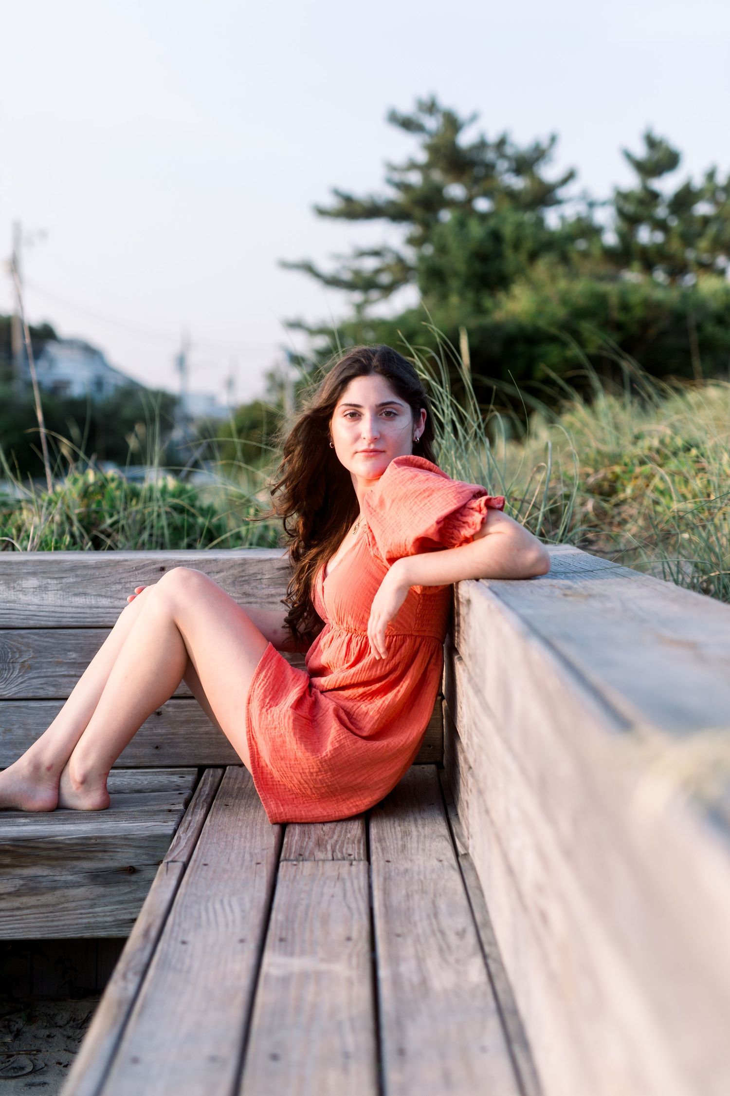Sunset portrait on wooden boardwalk wearing coral dress with pine trees in background.
