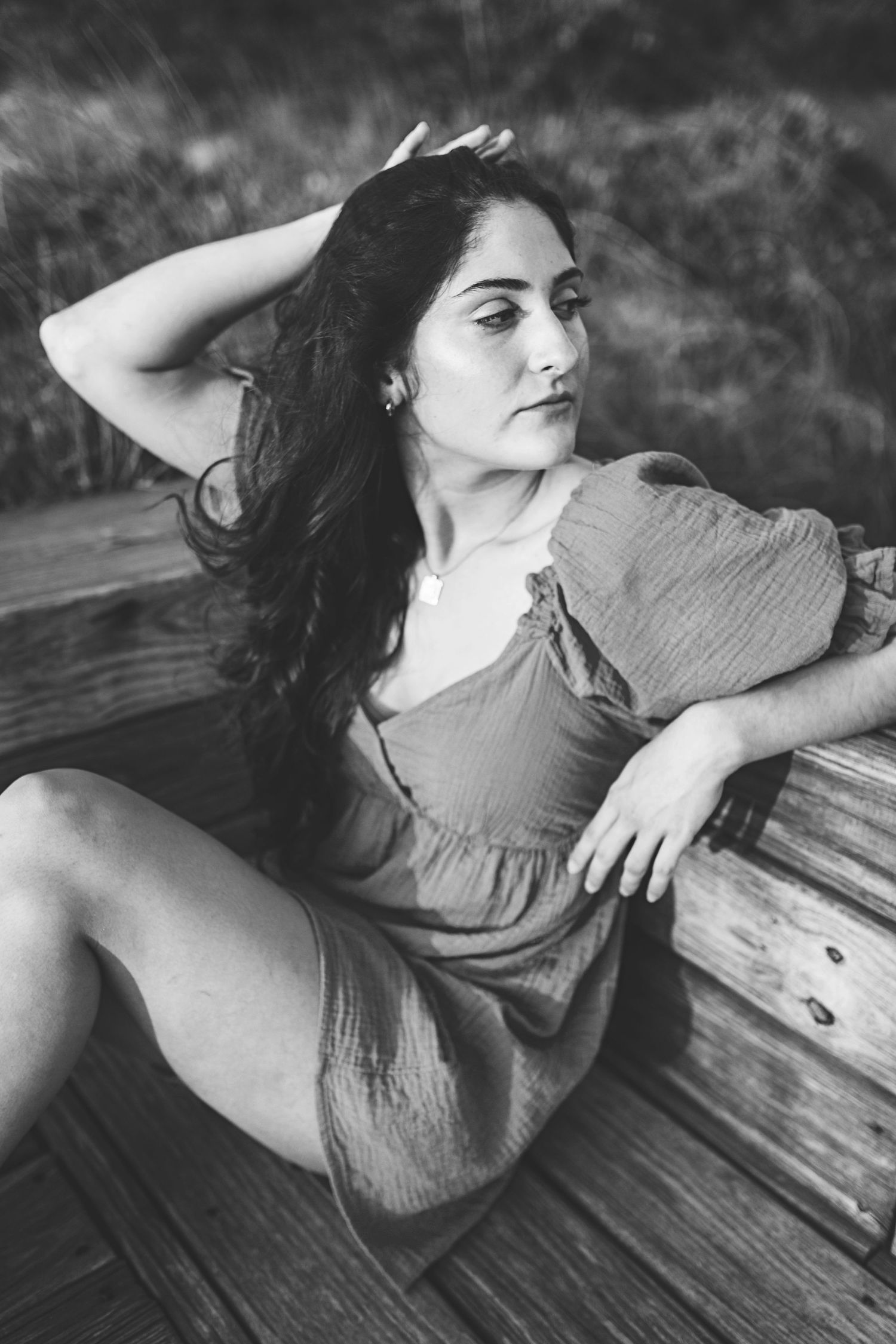 Black and white portrait showing figure in dress reclining on wooden surface in artistic pose.