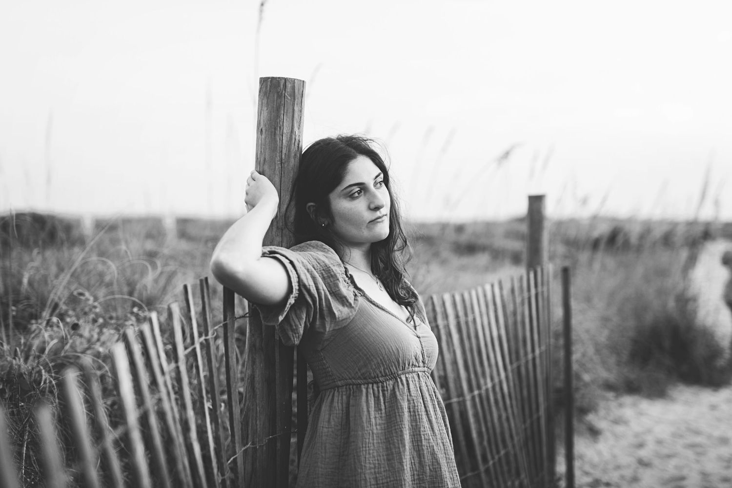 Monochrome portrait showing artistic pose against beach fence and posts.