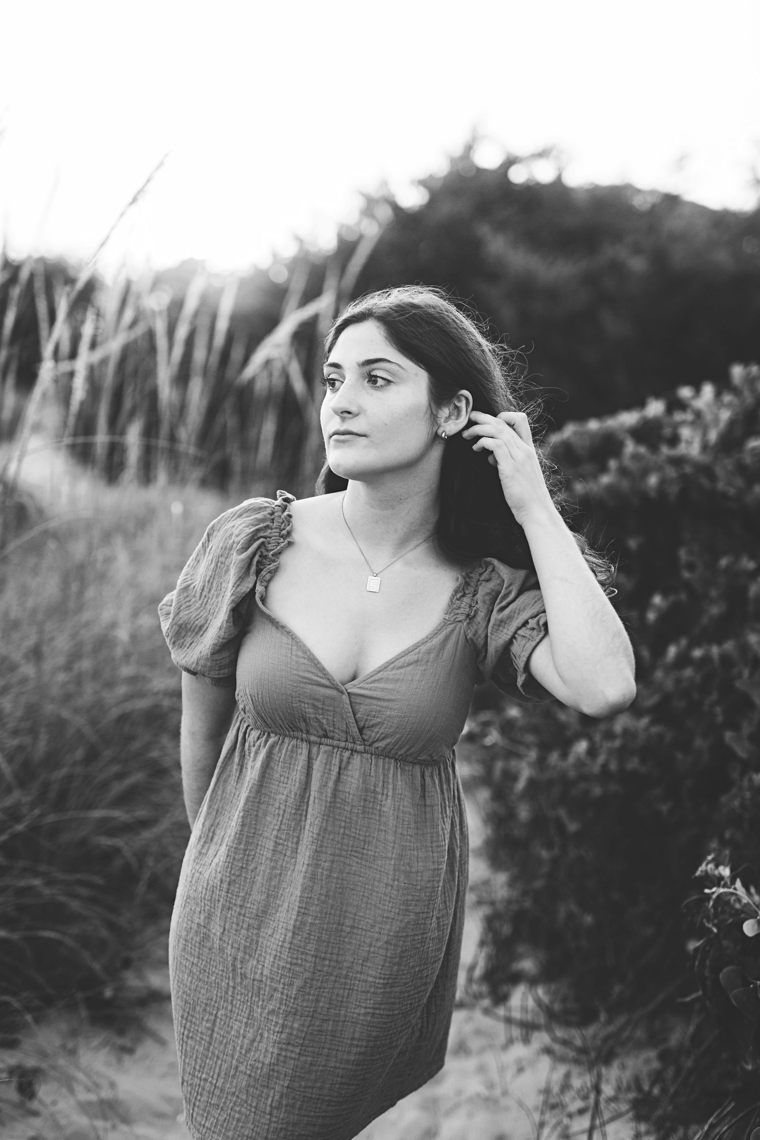 Person in empire-waist dress poses in natural setting with beach grass and shrubs.