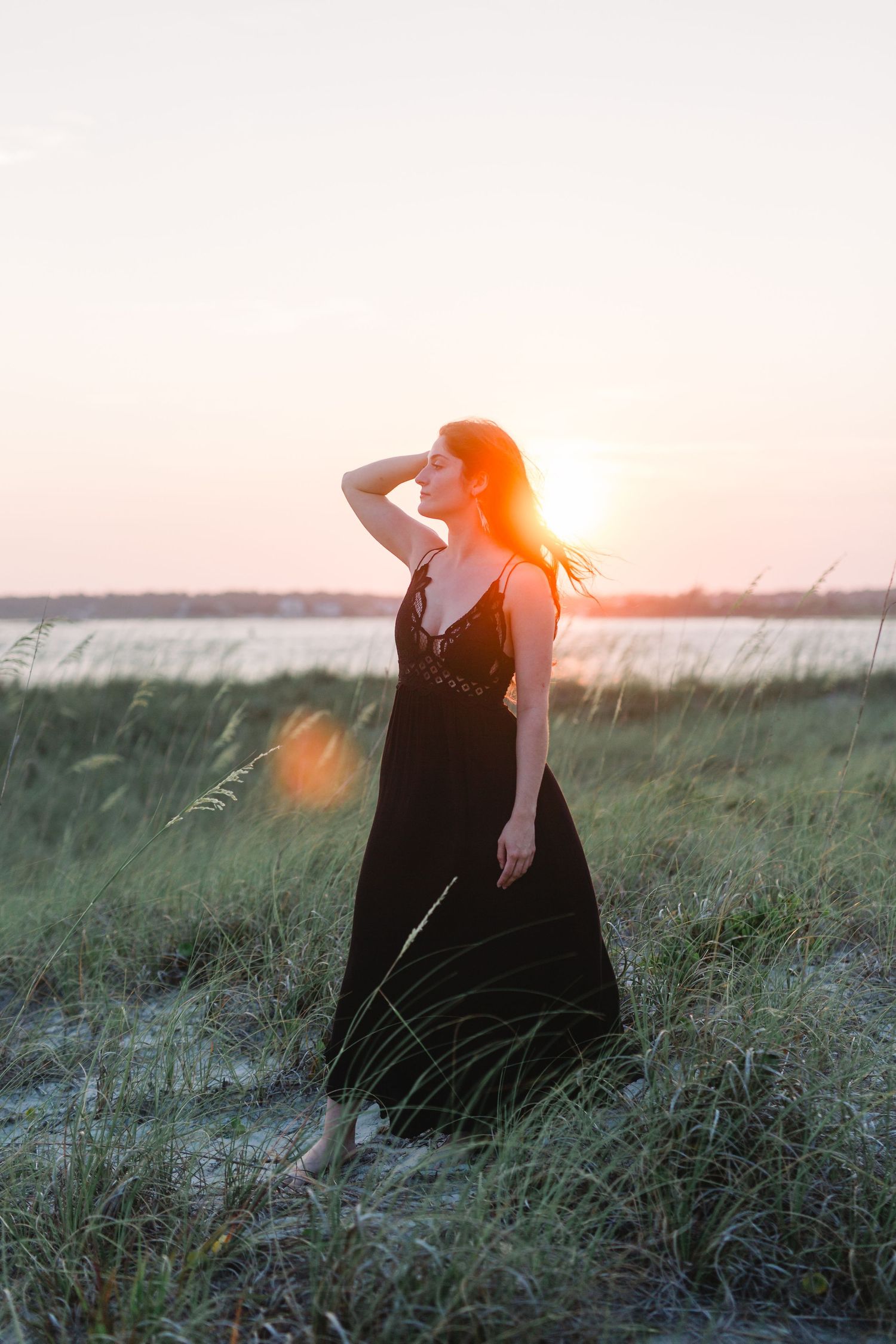 Silhouette in flowing dress poses against golden sunset over coastal waters.