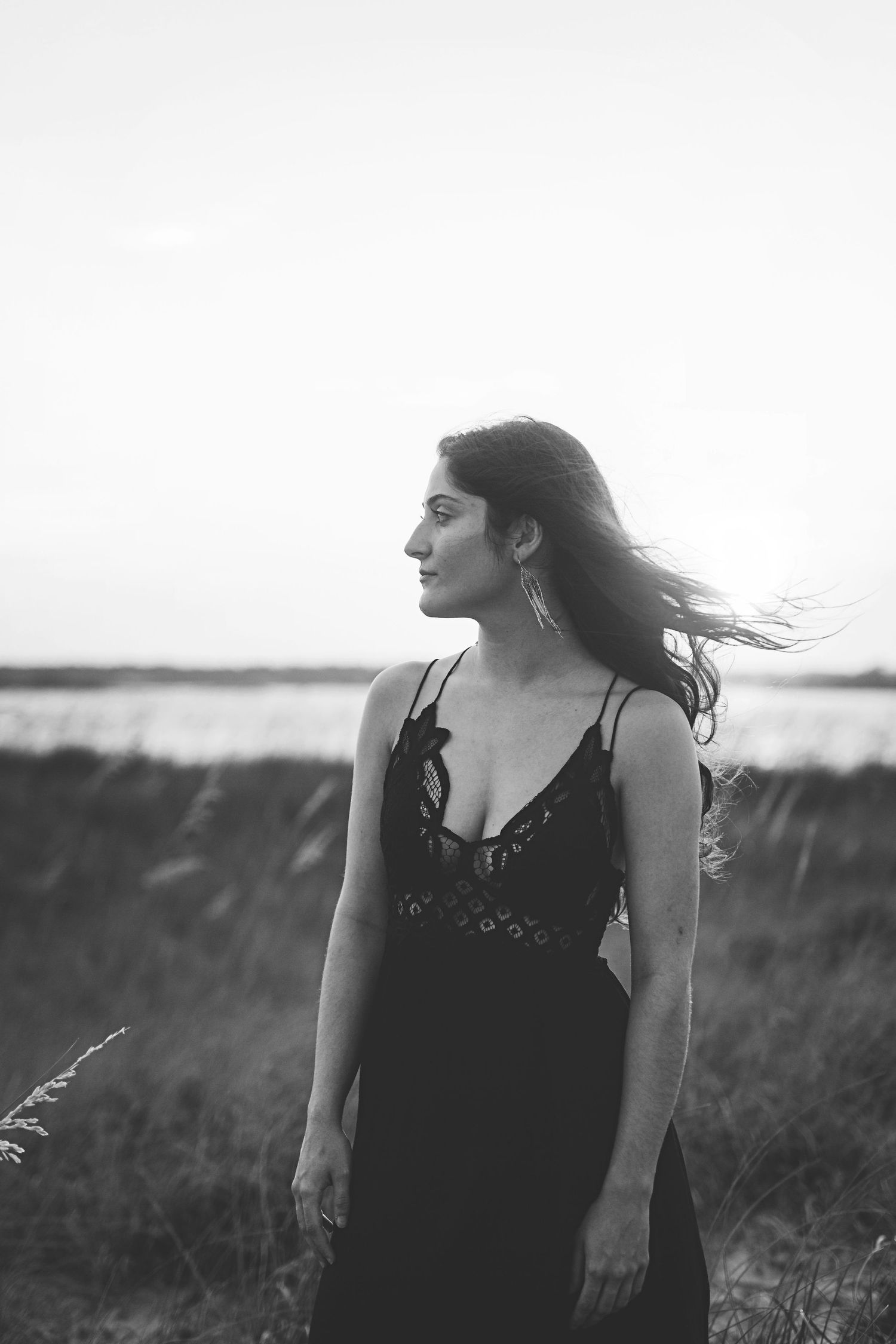 Profile view of person in black lace dress with wind-swept hair against coastal backdrop.