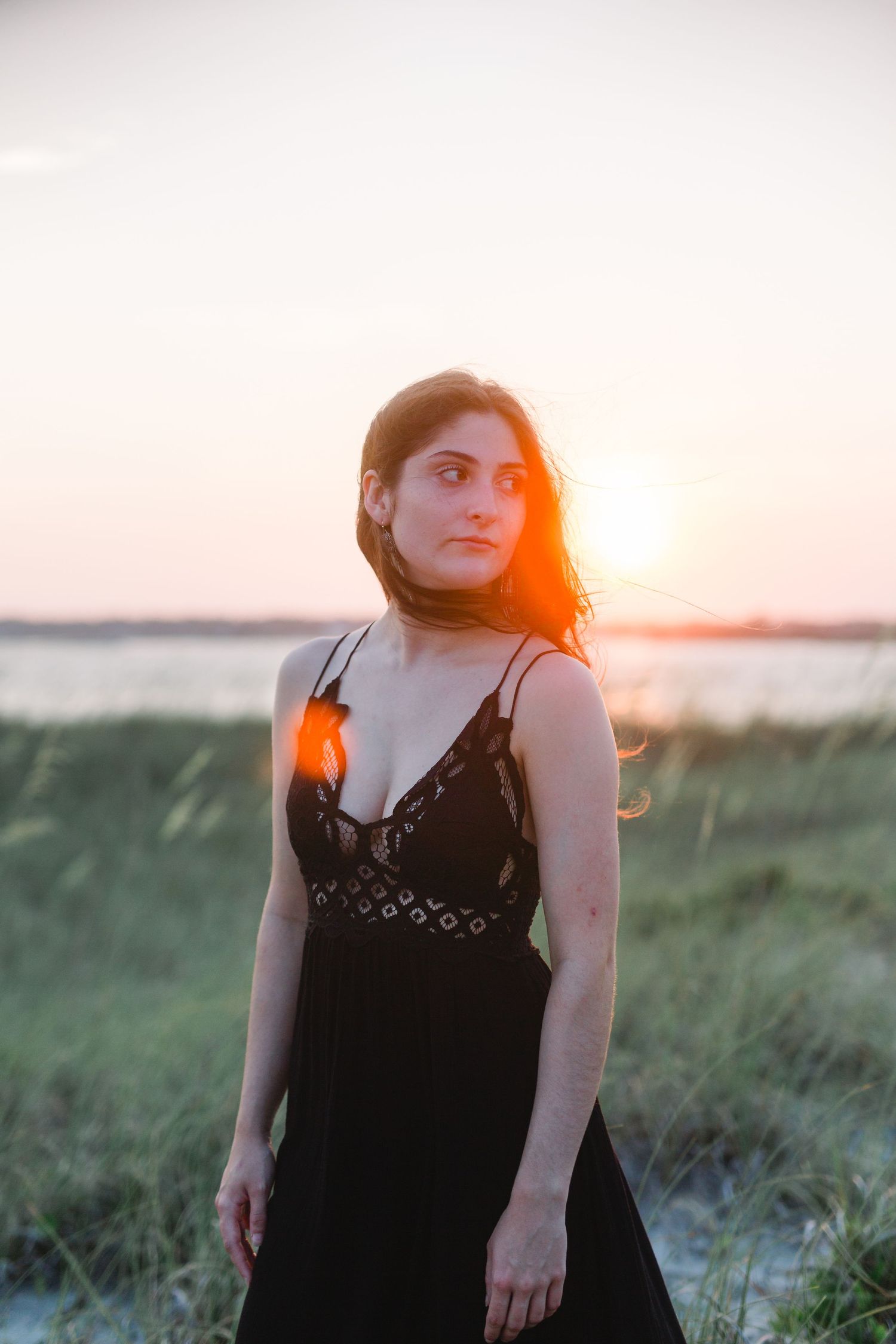 Person in black dress illuminated by sunset glow with coastal waters in background.