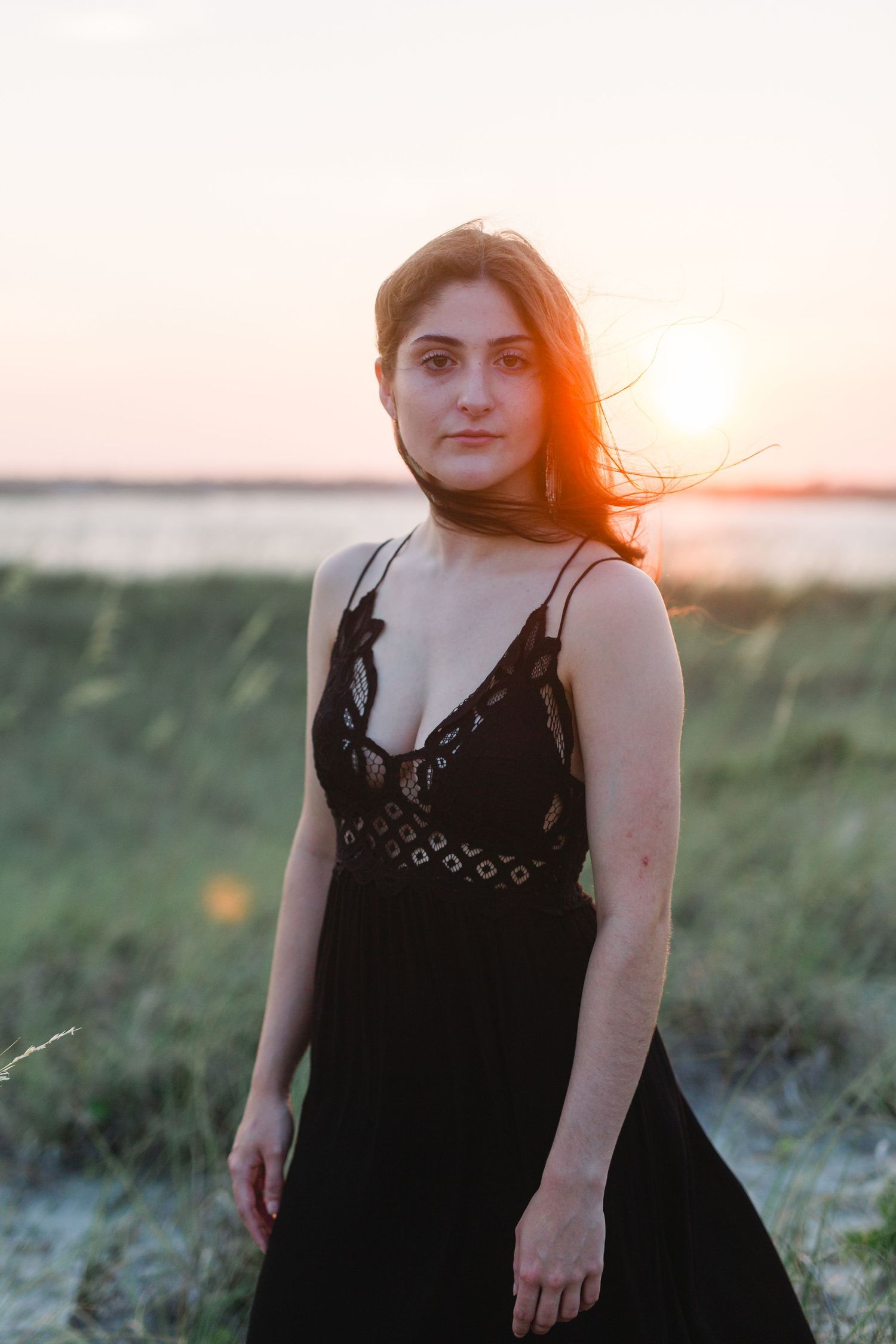 Sunset portrait with person wearing black dress against coastal landscape.