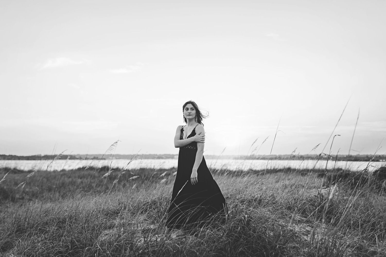 Black and white image of person in flowing dress standing in coastal grassland.
