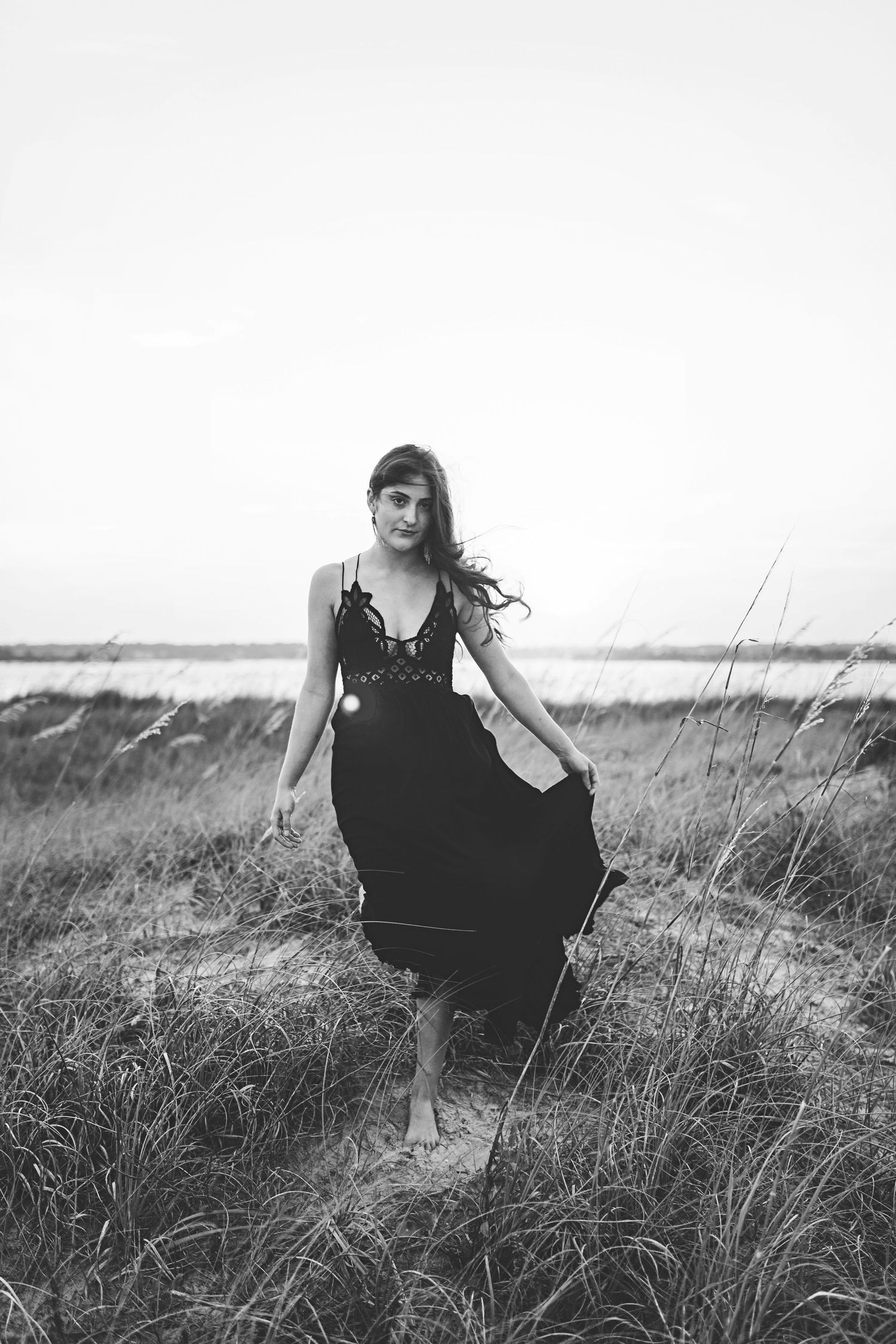 Black and white portrait of someone standing barefoot in windswept coastal grass.