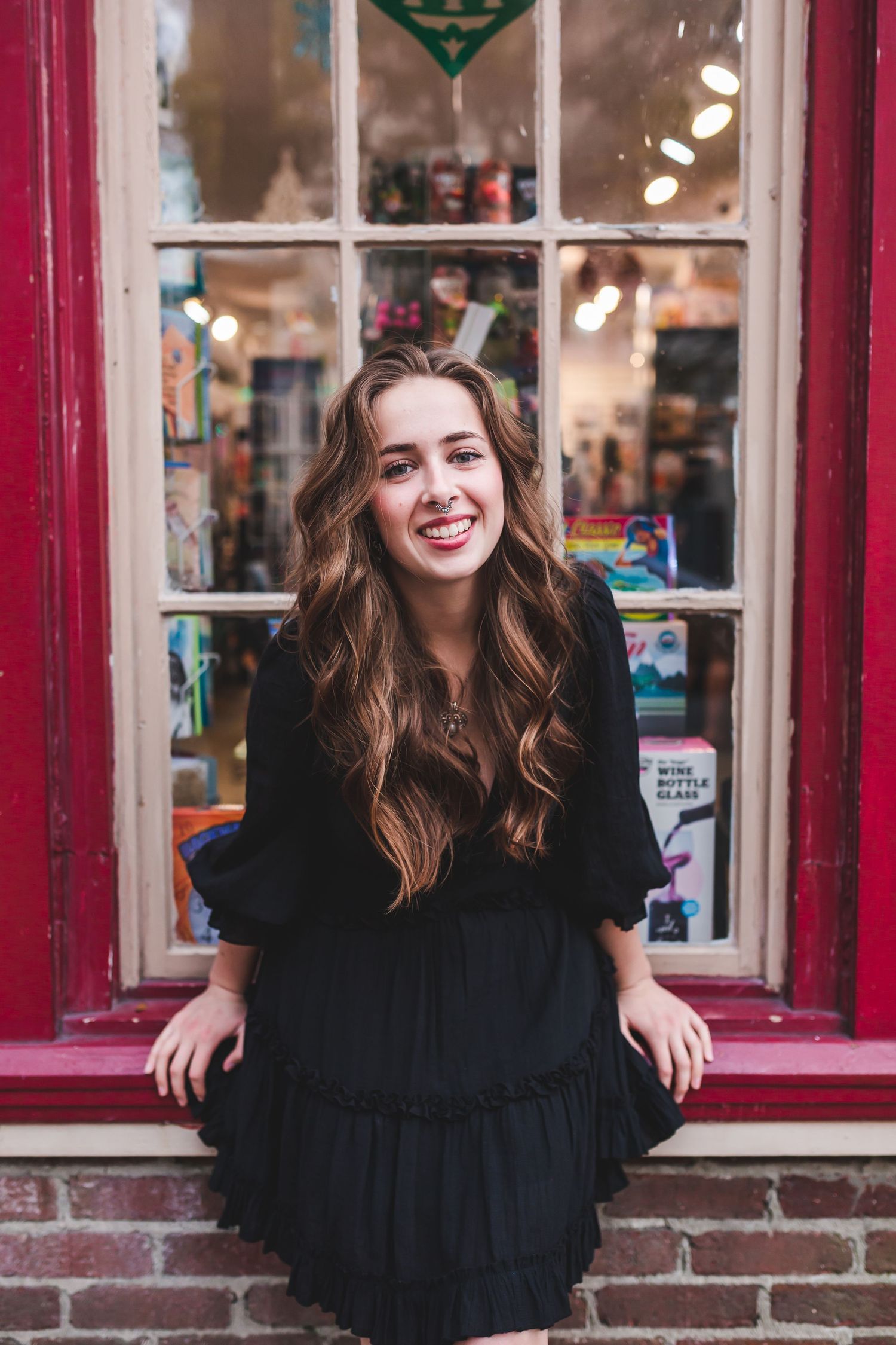 Casual portrait by vintage shop window with red trim and holiday displays.