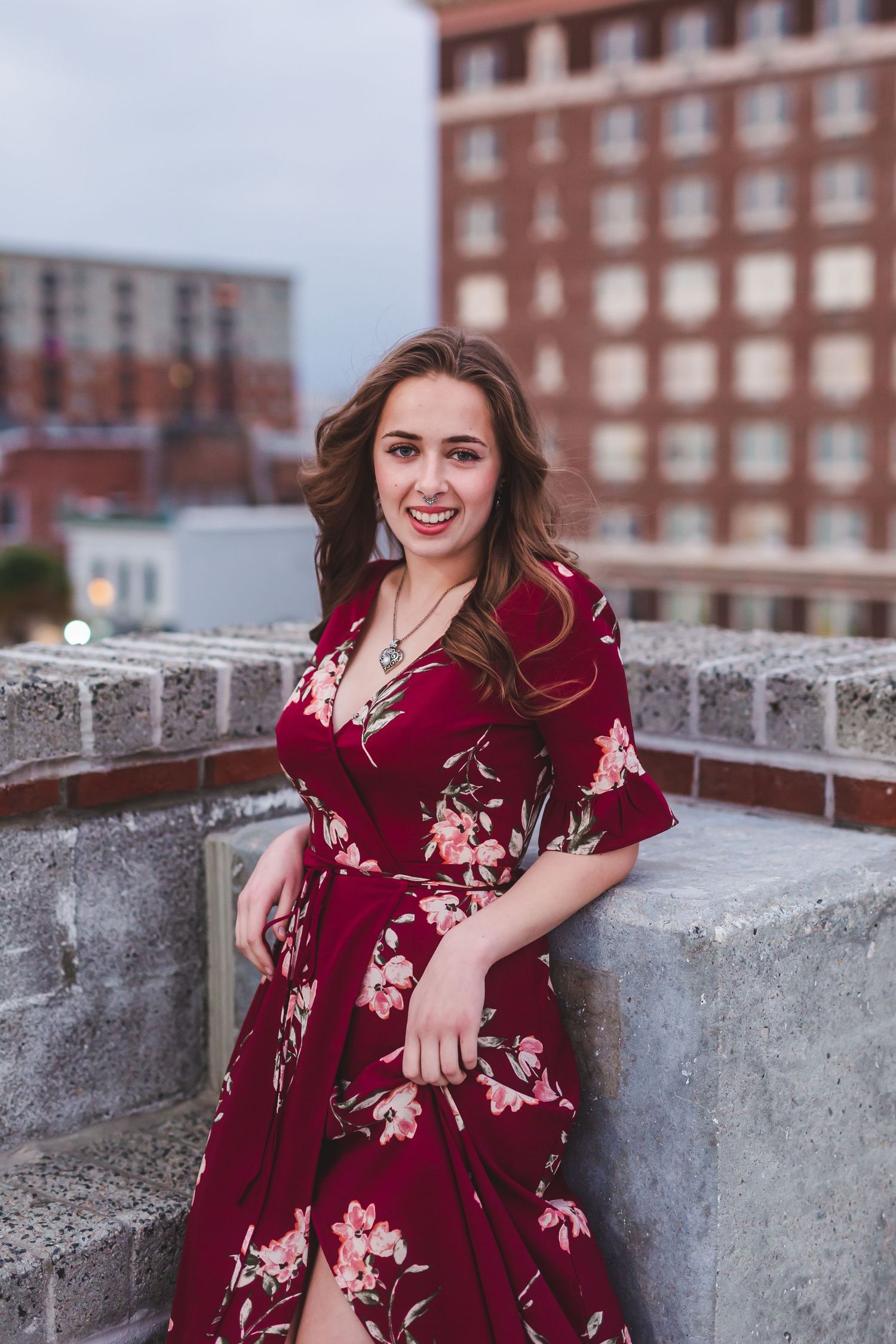 Woman in burgundy floral dress standing by concrete wall on urban rooftop.