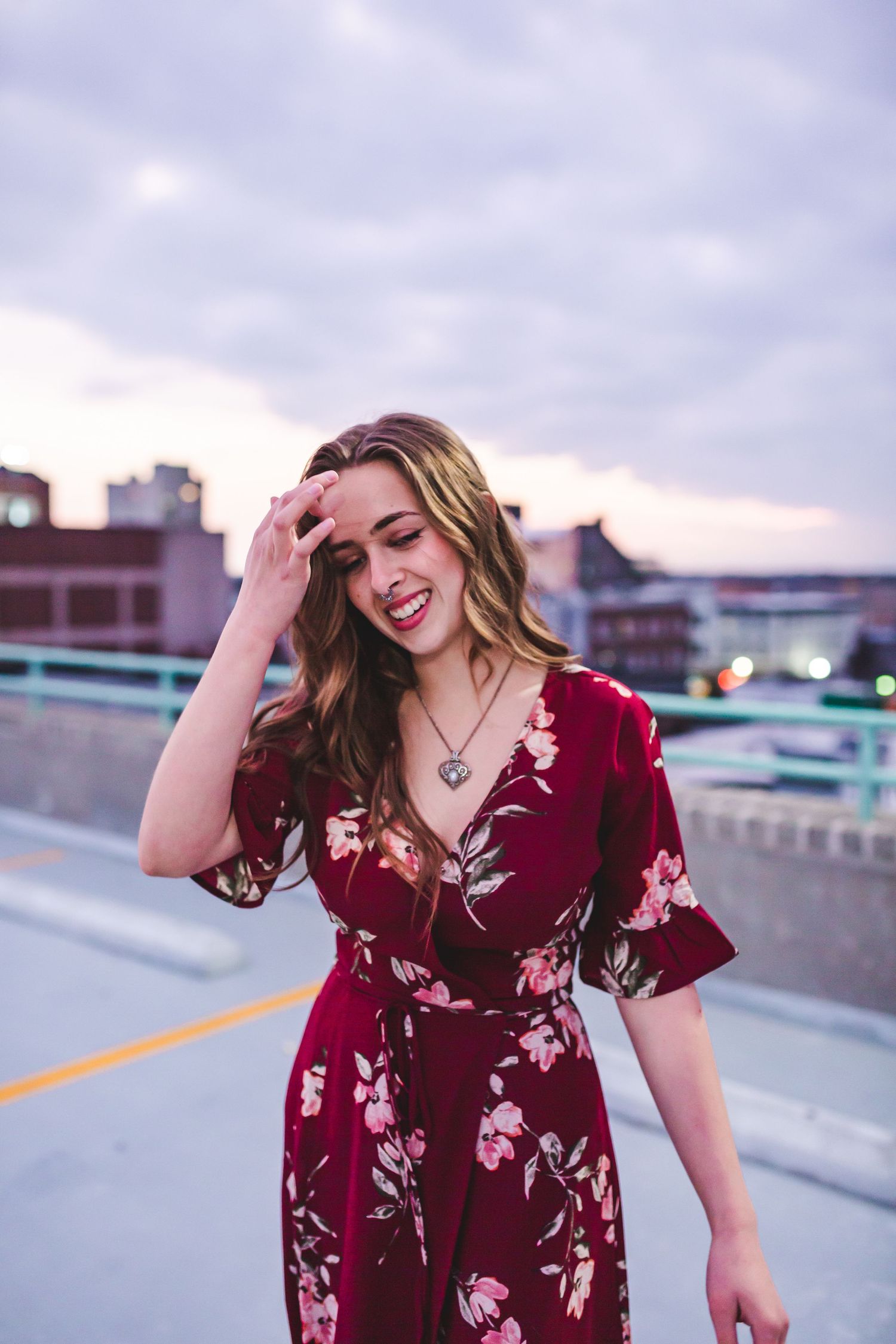 Candid portrait of woman in floral wrap dress on rooftop parking structure.