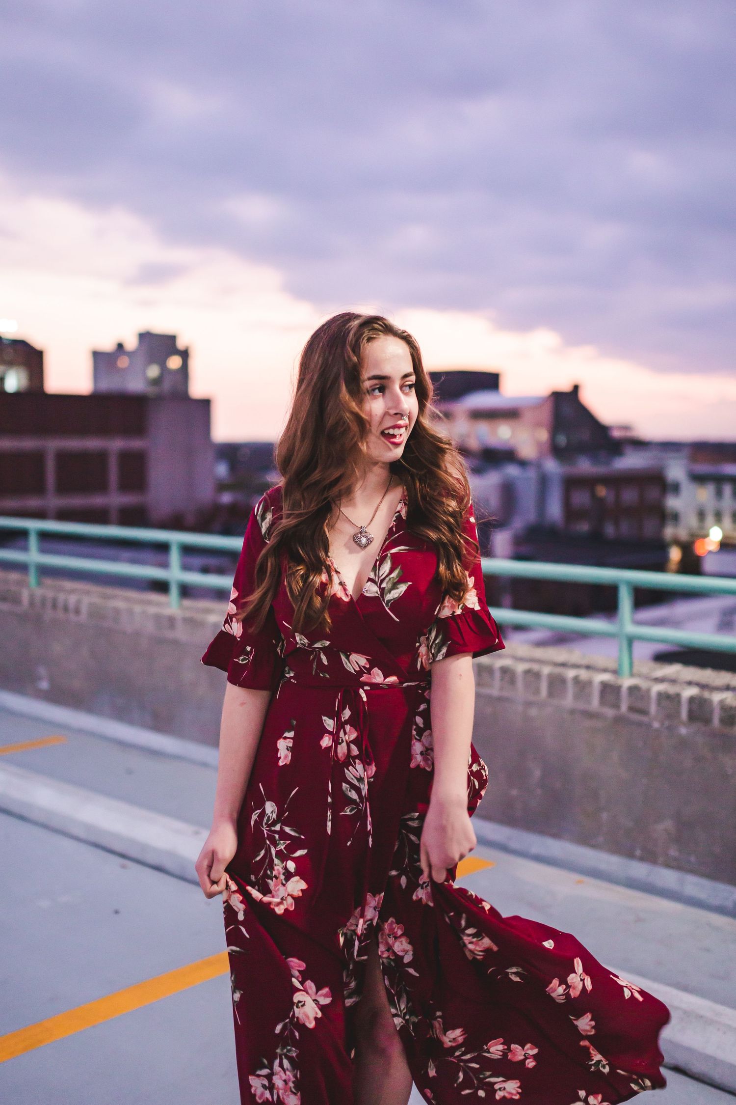 Joyful outdoor fashion portrait featuring burgundy floral maxi dress against city backdrop.