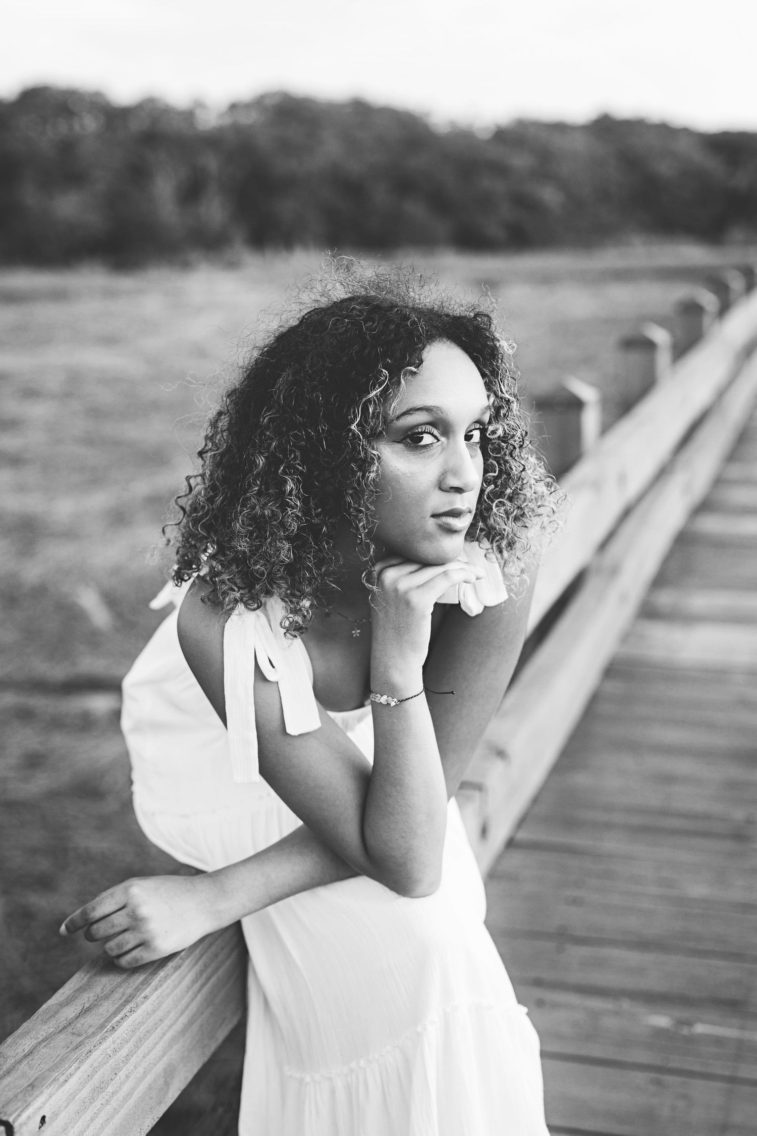 A monochrome portrait capturing a contemplative pose against a coastal boardwalk setting.