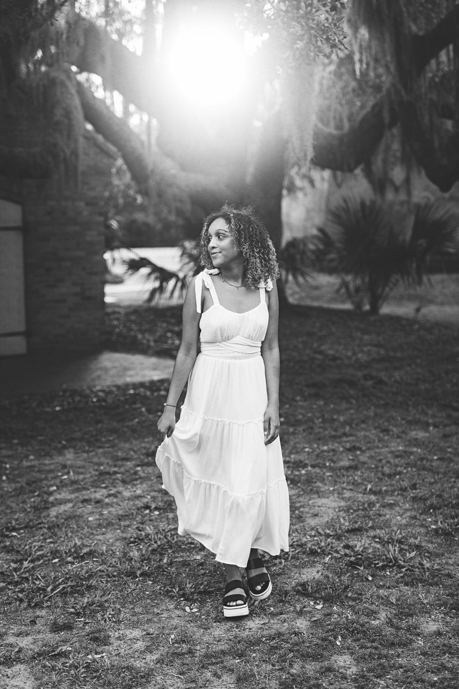 Black and white photo of woman in white dress standing in garden with sunburst effect.