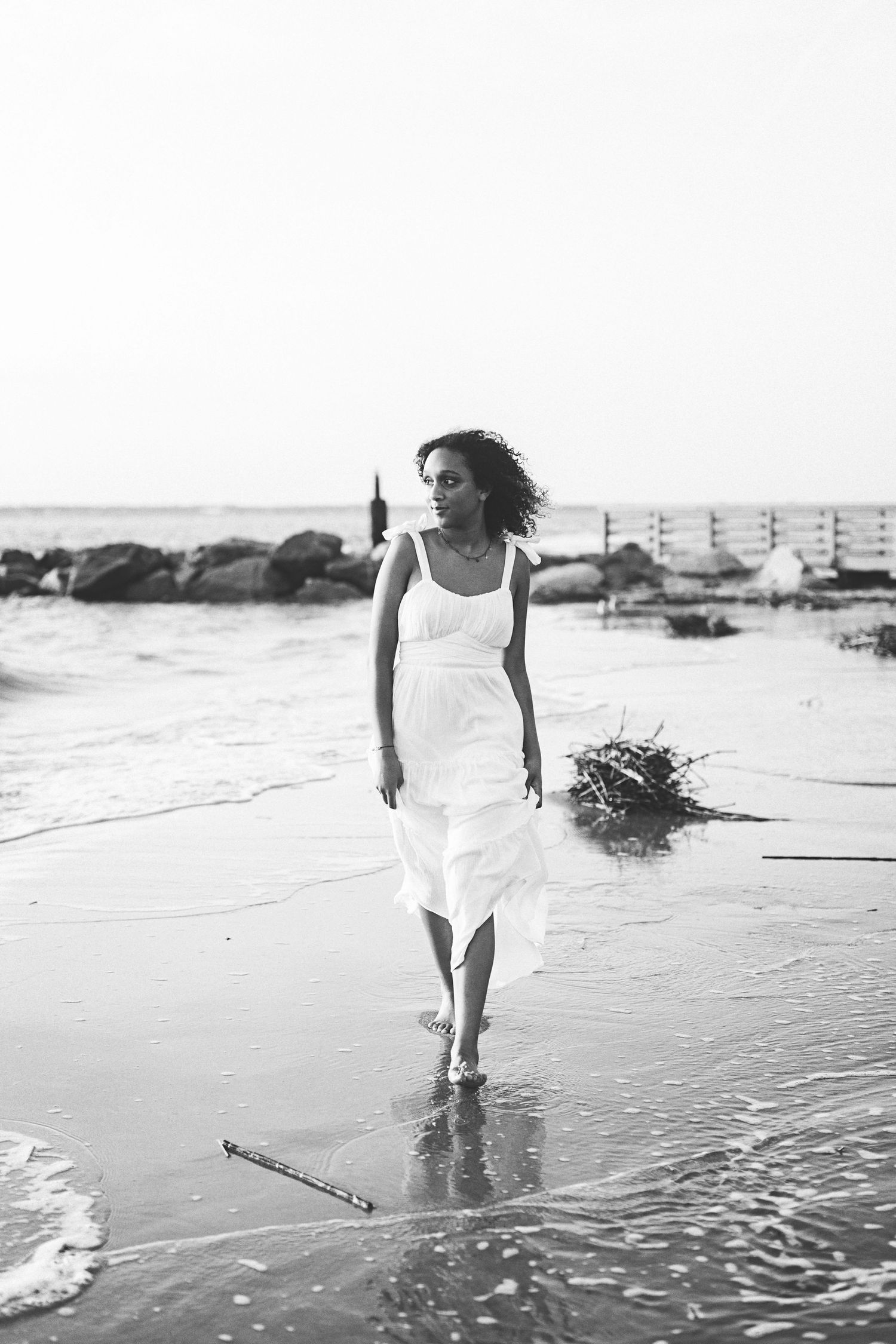 Black and white beach photo of a flowing white dress against coastal rocks and waves.