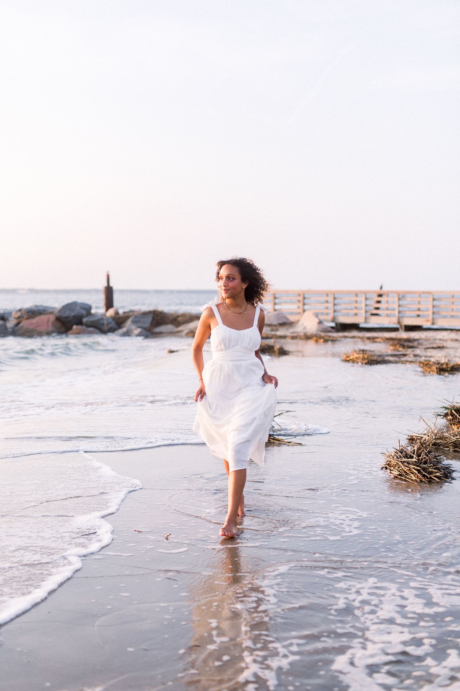 A carefree beach scene with white dress flowing in ocean breeze at sunset.