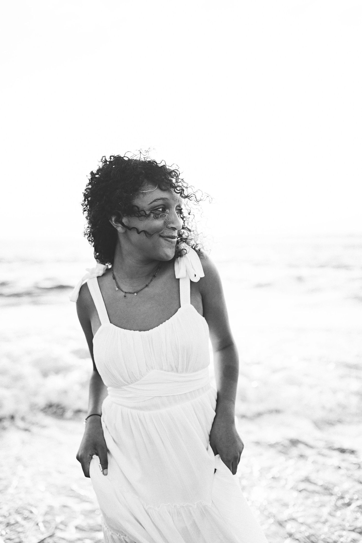 Black and white beachside portrait showcasing curly hair and white sundress.