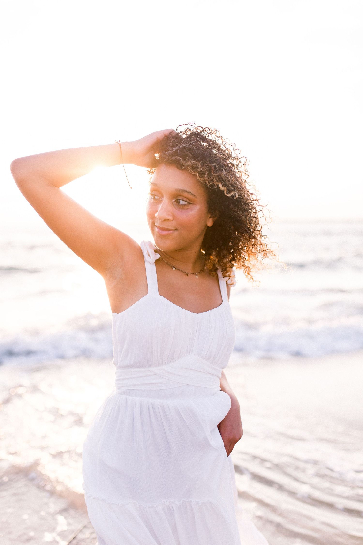 Sunset beach portrait with golden light illuminating white dress and natural curls.