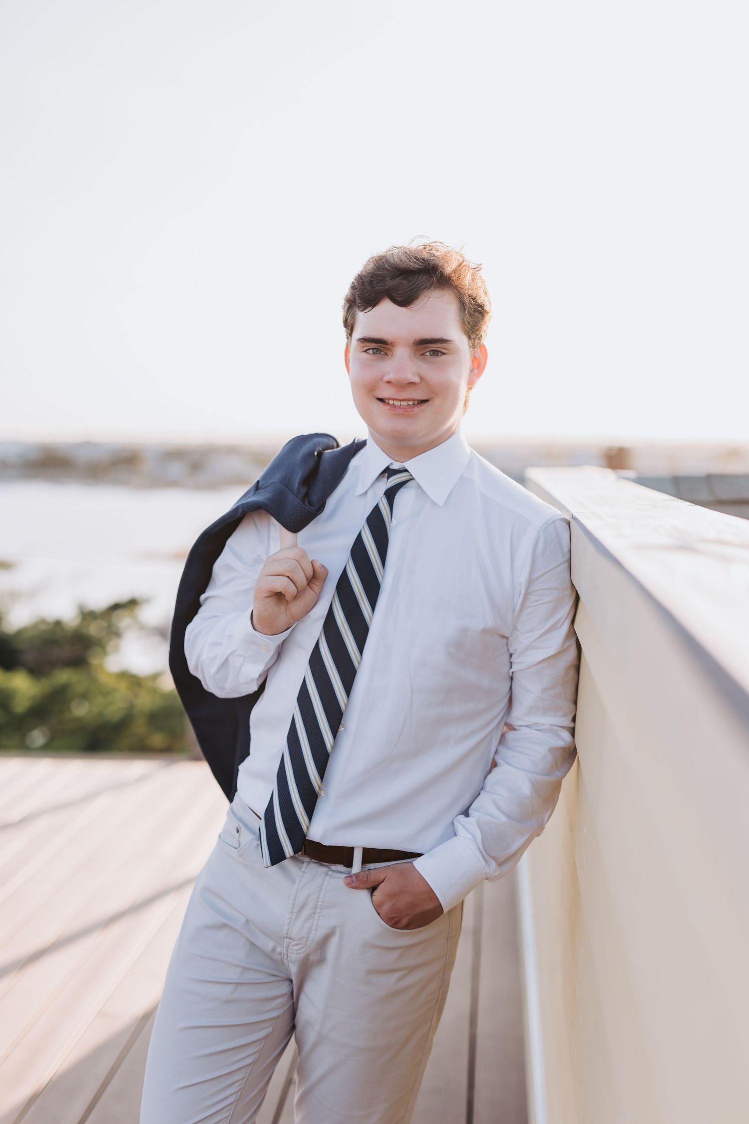 Portrait of someone in business attire with striped tie holding suit jacket over shoulder.