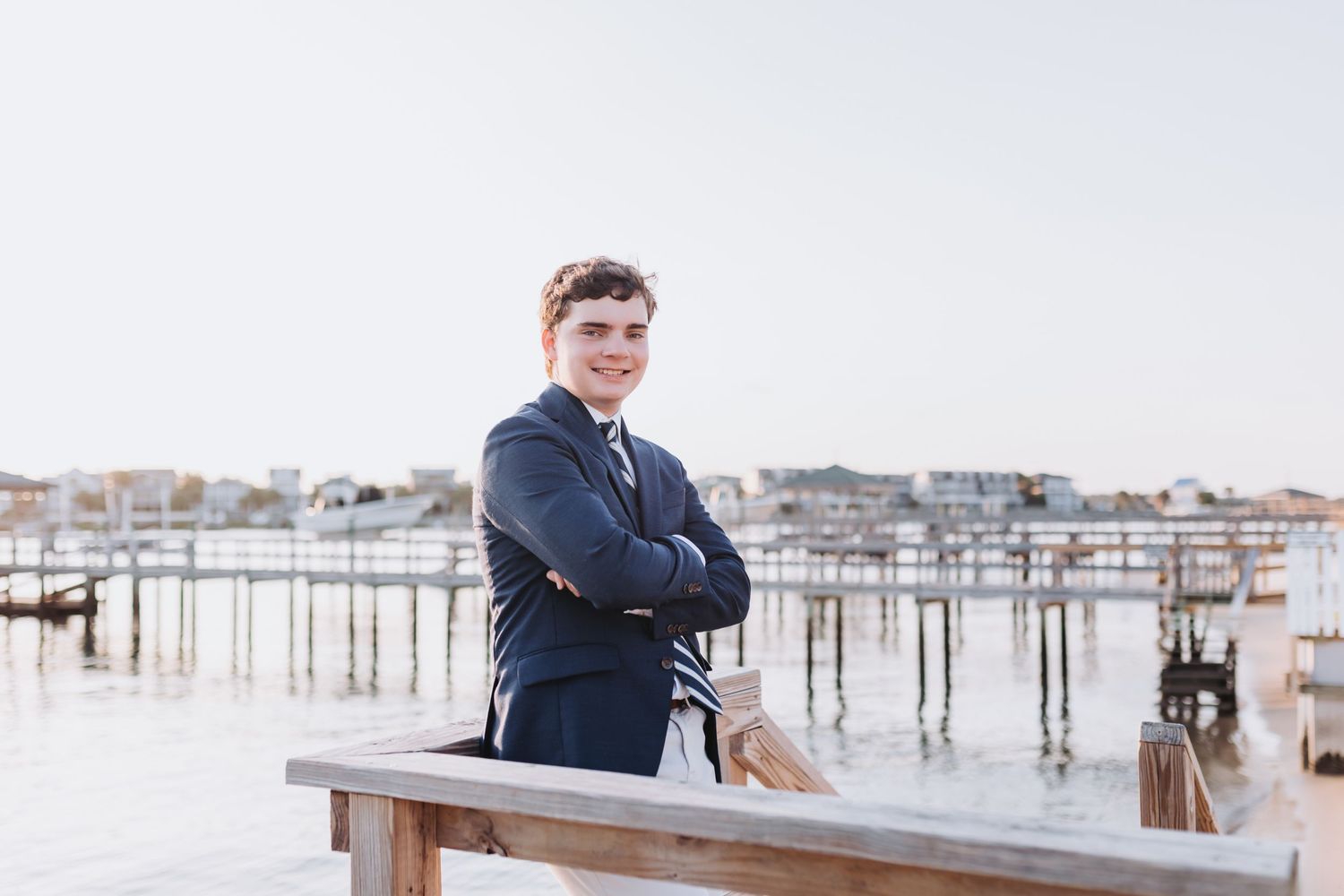 Portrait on coastal dock with crossed arms wearing navy blazer with waterfront backdrop.