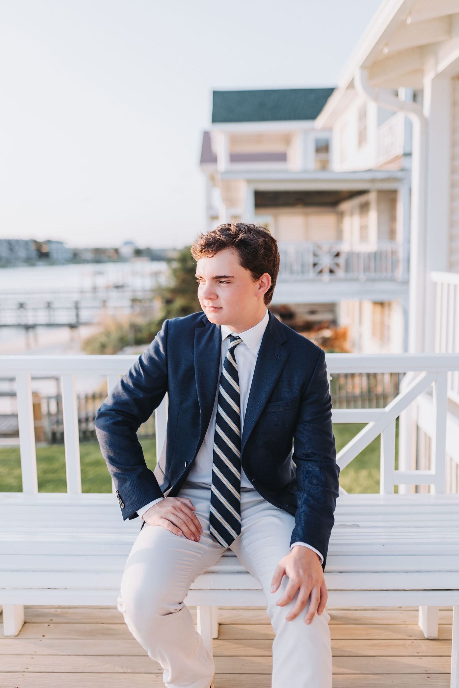 Formal portrait on seaside deck wearing navy blazer and striped tie with coastal view.