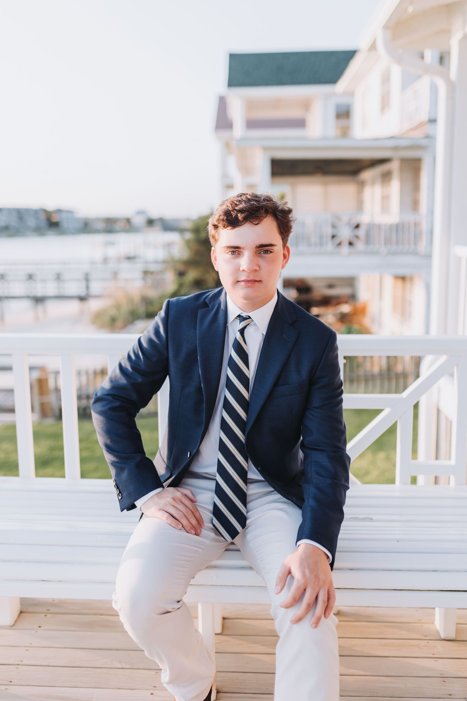 A preppy coastal photoshoot featuring a navy blazer and striped tie on a waterfront deck.