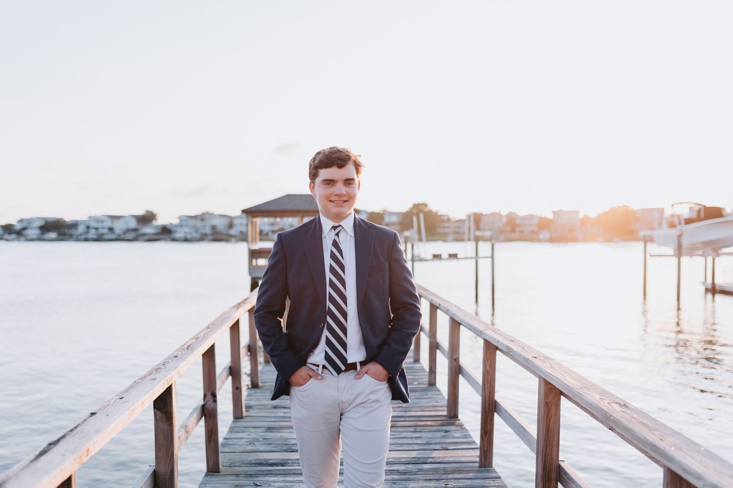 Professional portrait on wooden dock with waterfront backdrop at sunset.