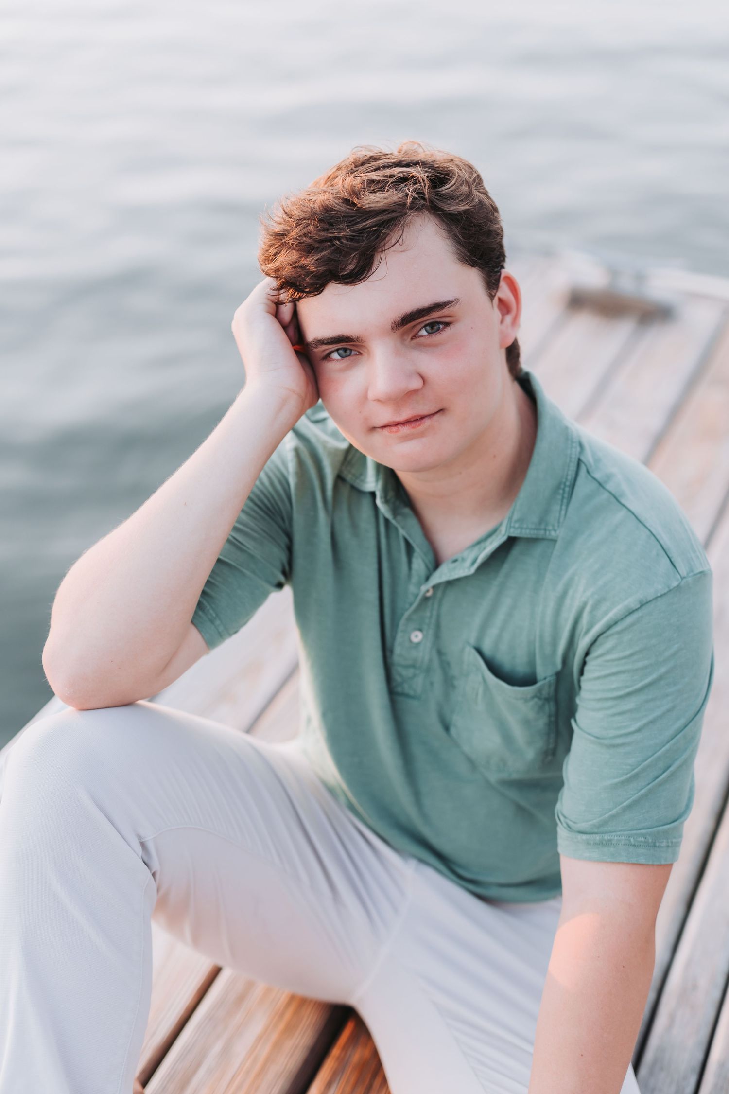 Relaxed seaside portrait in green polo shirt on wooden dock.