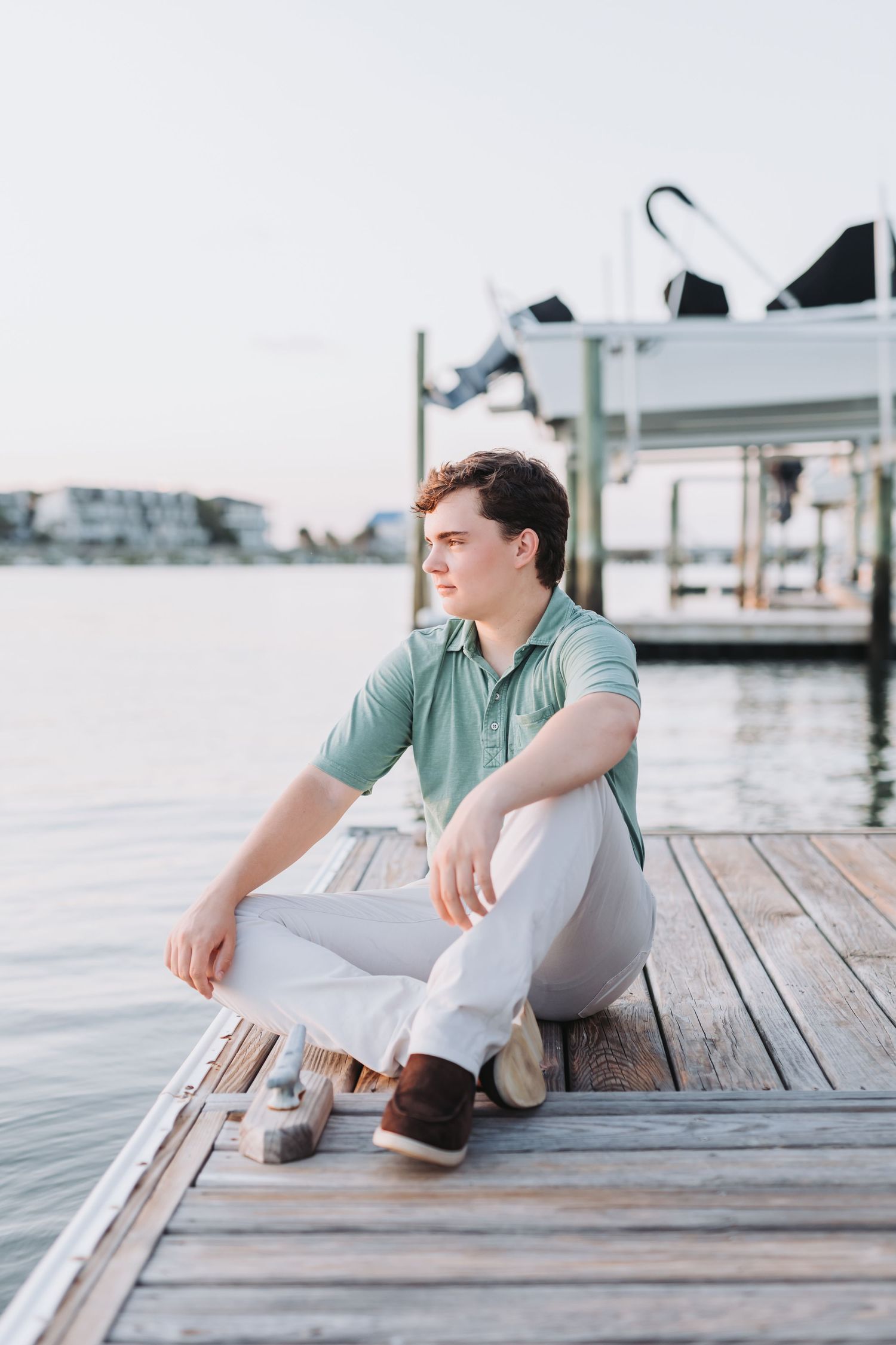 Casual waterfront pose in mint green polo on wooden pier.