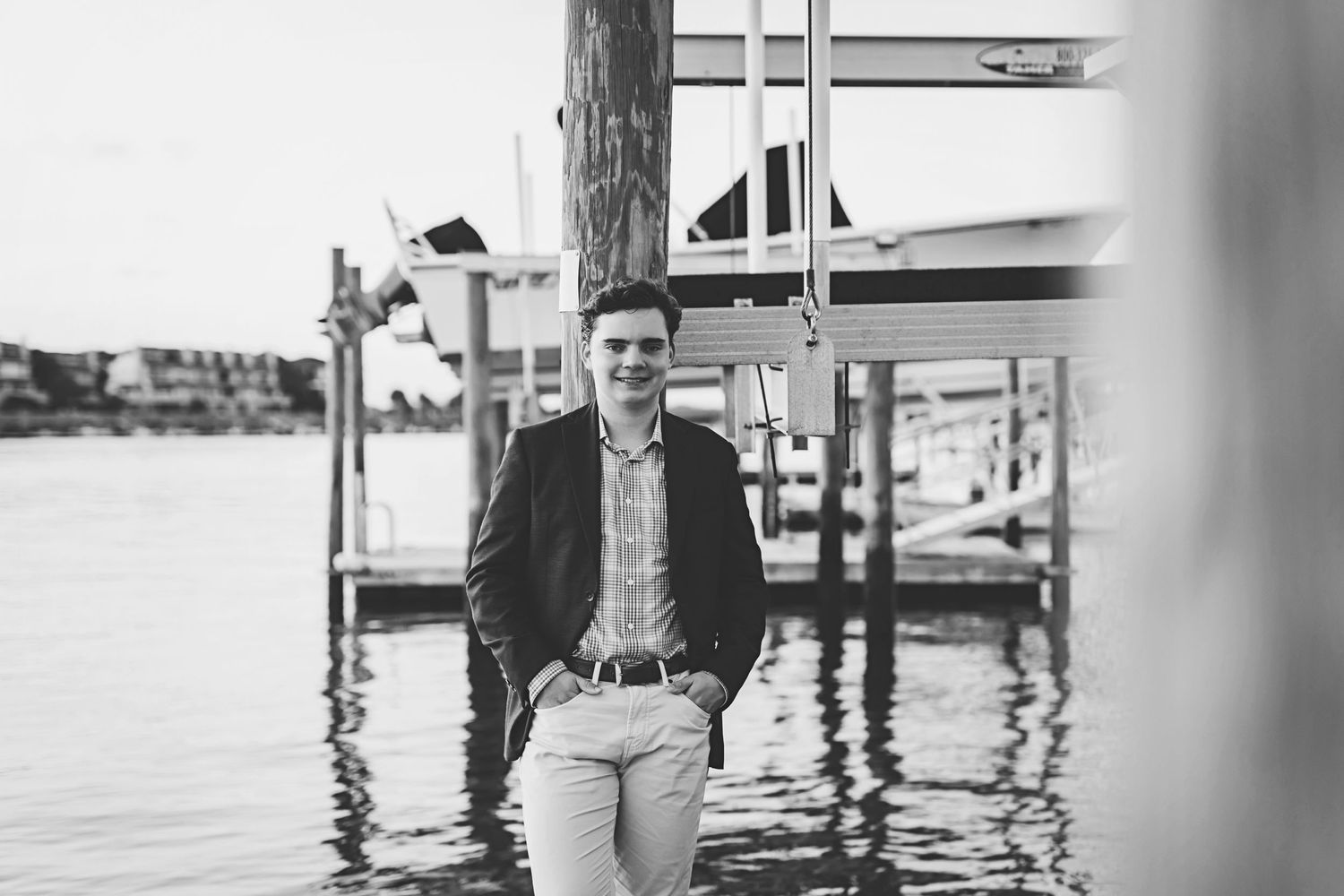 Casual portrait by boat docks wearing a navy blazer and checkered shirt.