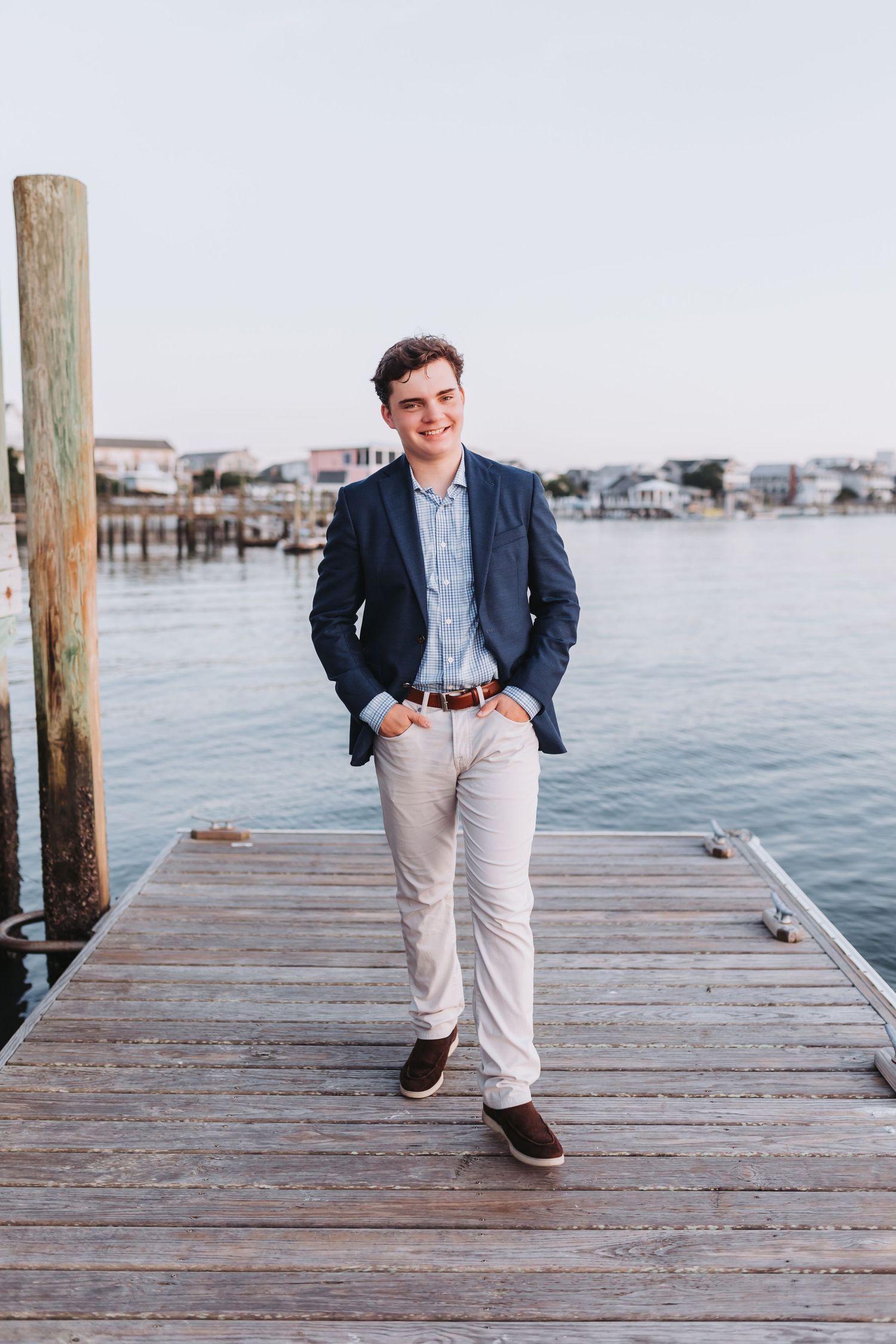 Professional portrait of someone in a navy blazer and khakis standing casually on a waterfront dock.