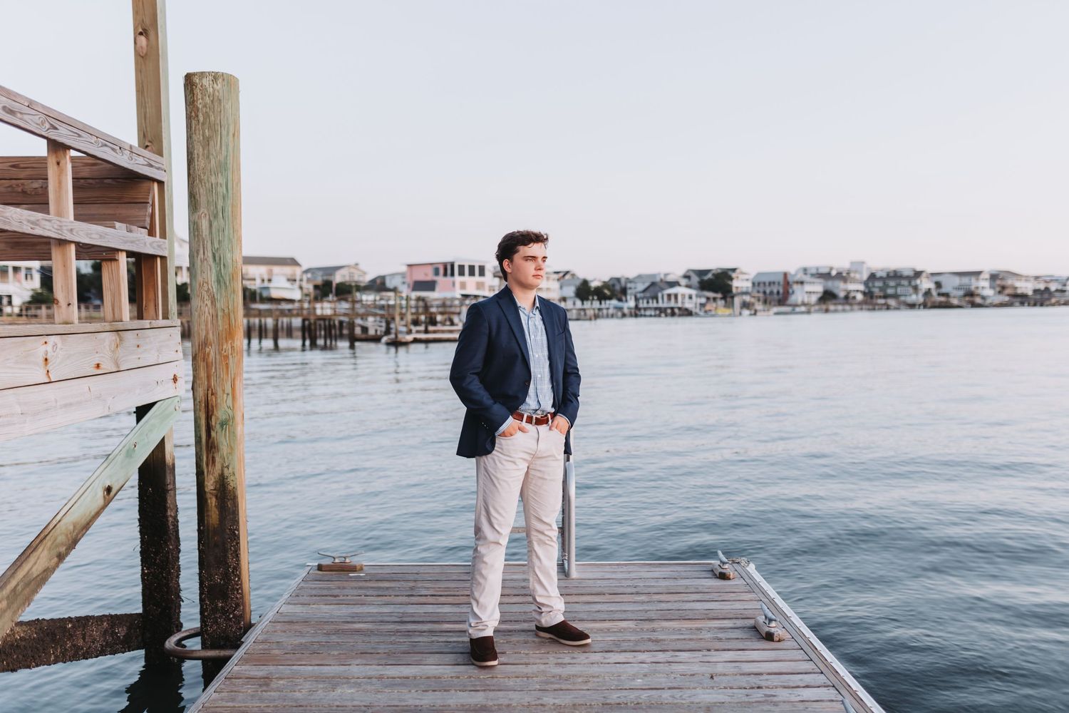 Outdoor portrait on a wooden pier with coastal homes and boats in the background.