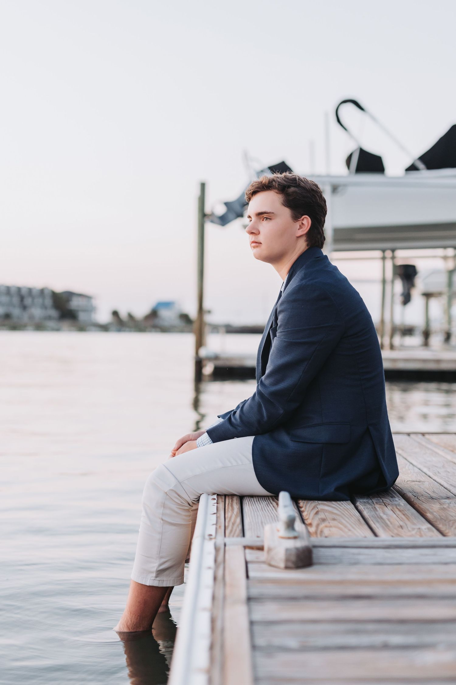 Side view portrait of someone sitting on a dock edge wearing a navy blazer at sunset.
