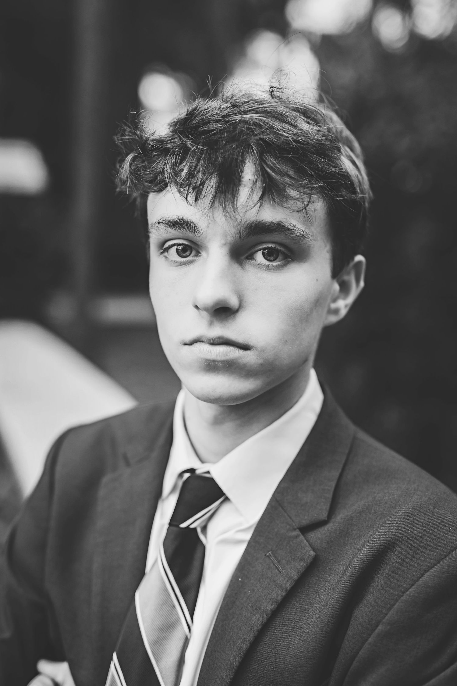 Black and white portrait of a person in a suit with a striped tie against a blurred background.