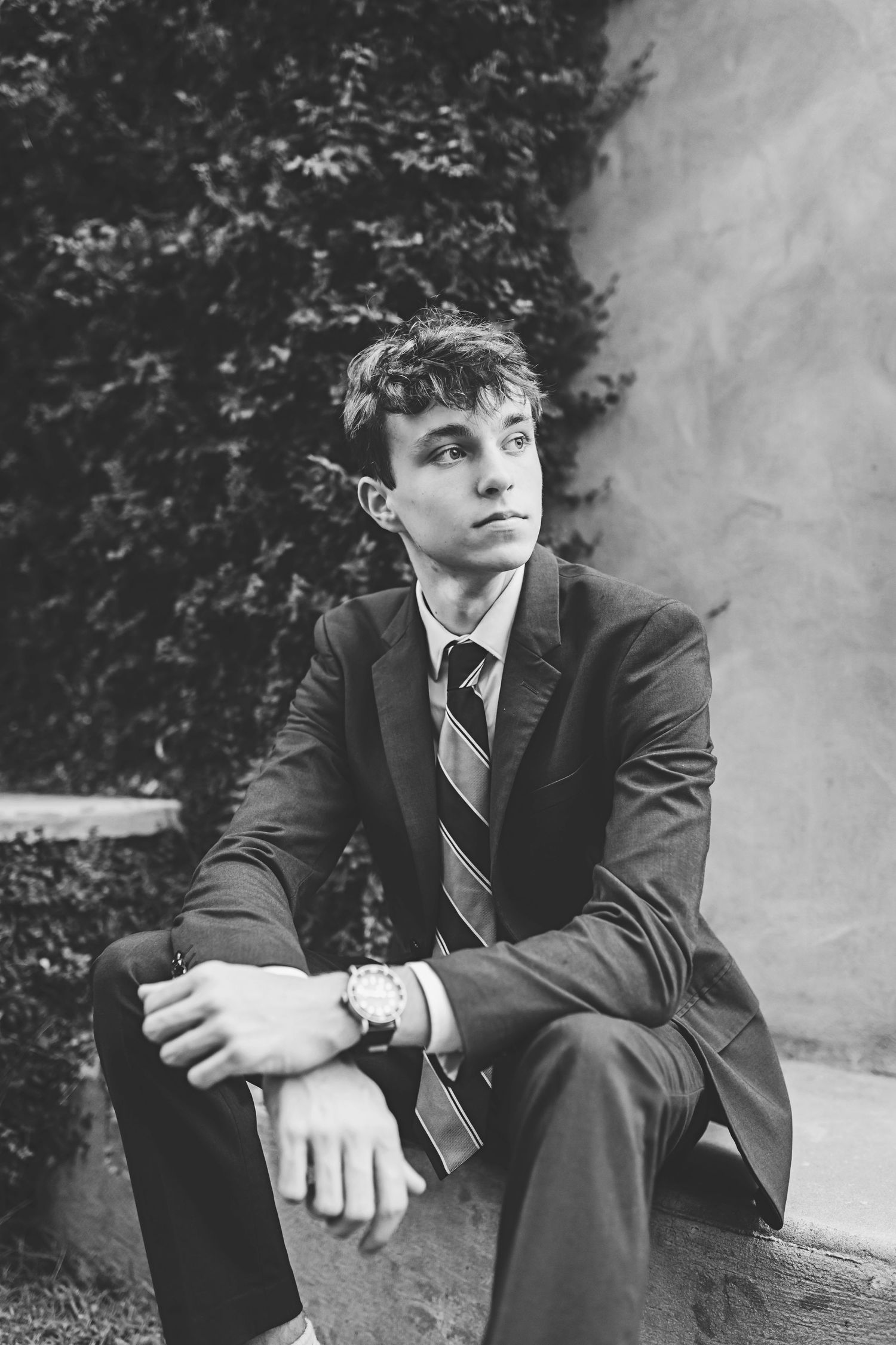 A person in formal attire sits thoughtfully on stone steps in a black and white photo.