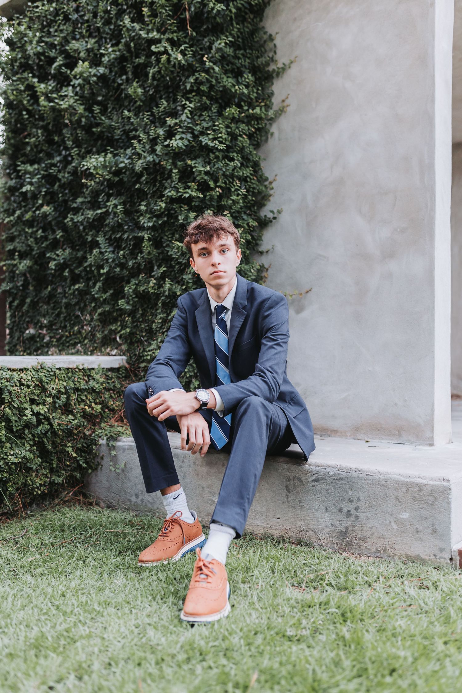 Business attire portrait with tan shoes against greenery and concrete wall.