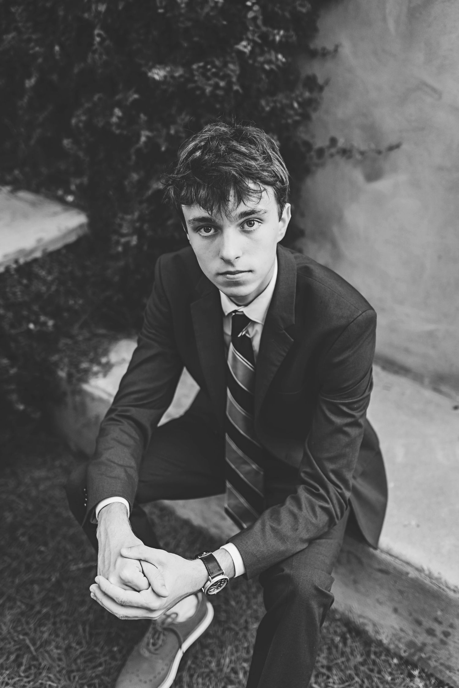 Black and white photo of a person in a suit crouching on garden steps.
