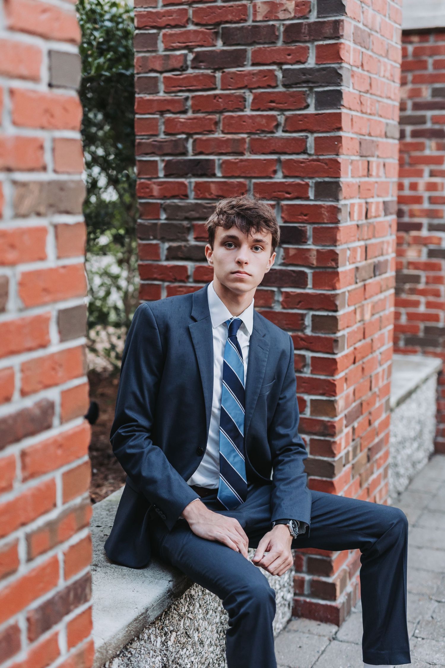 Professional portrait against red brick wall wearing navy suit and striped tie.